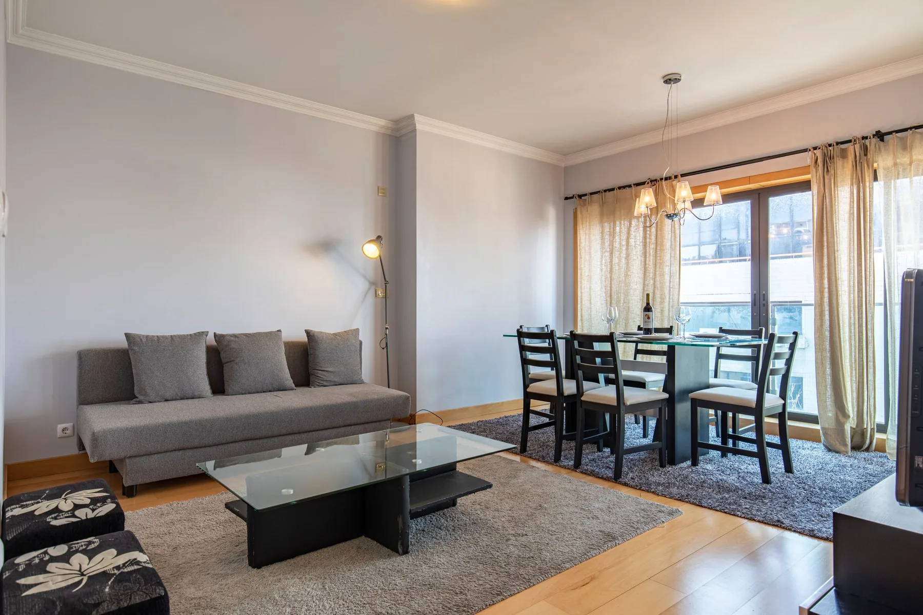 Una sala de estar con asientos, una mesa de centro de vidrio y un comedor junto a las ventanas.
