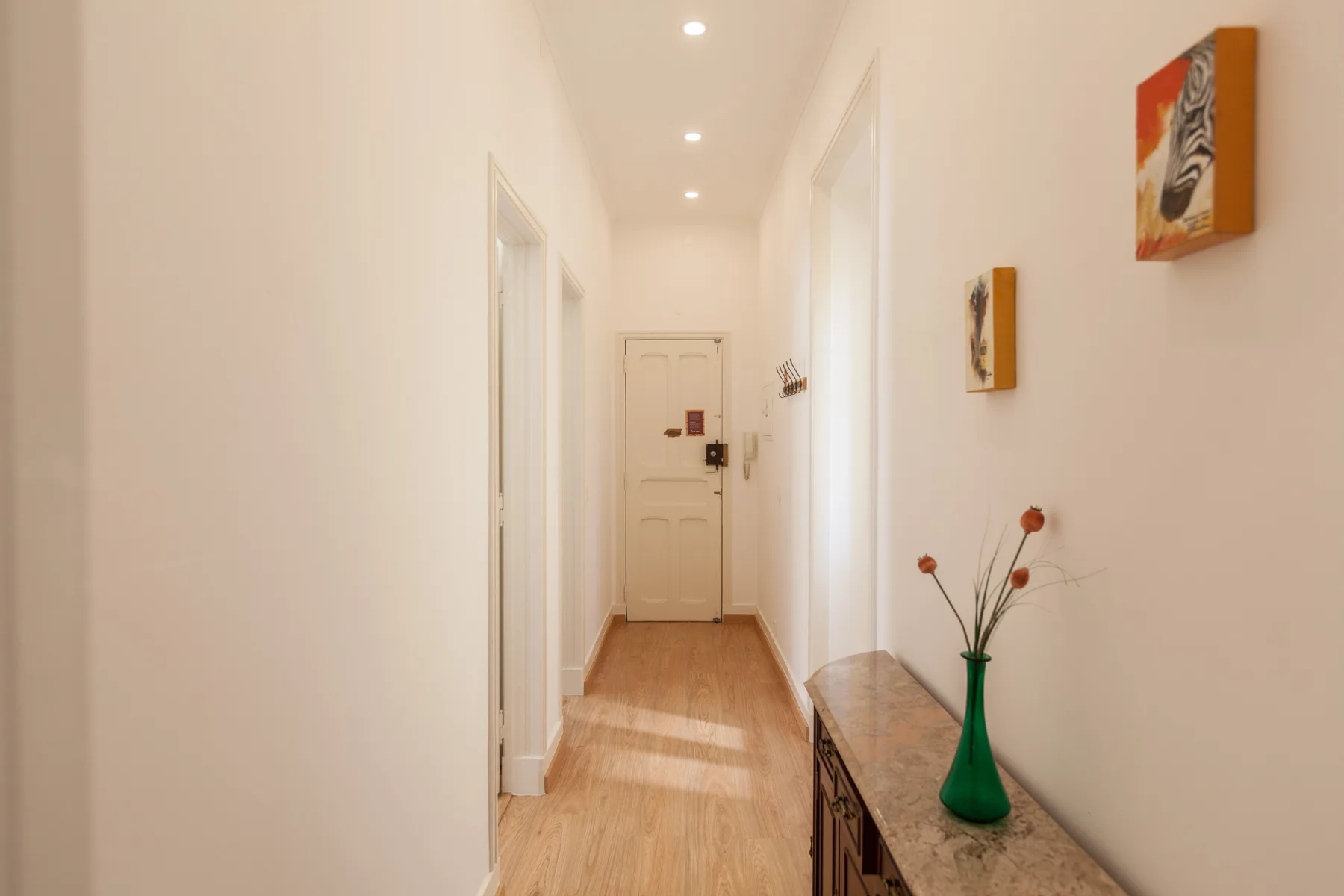 Un pasillo luminoso con suelo de madera clara y cuadros enmarcados.