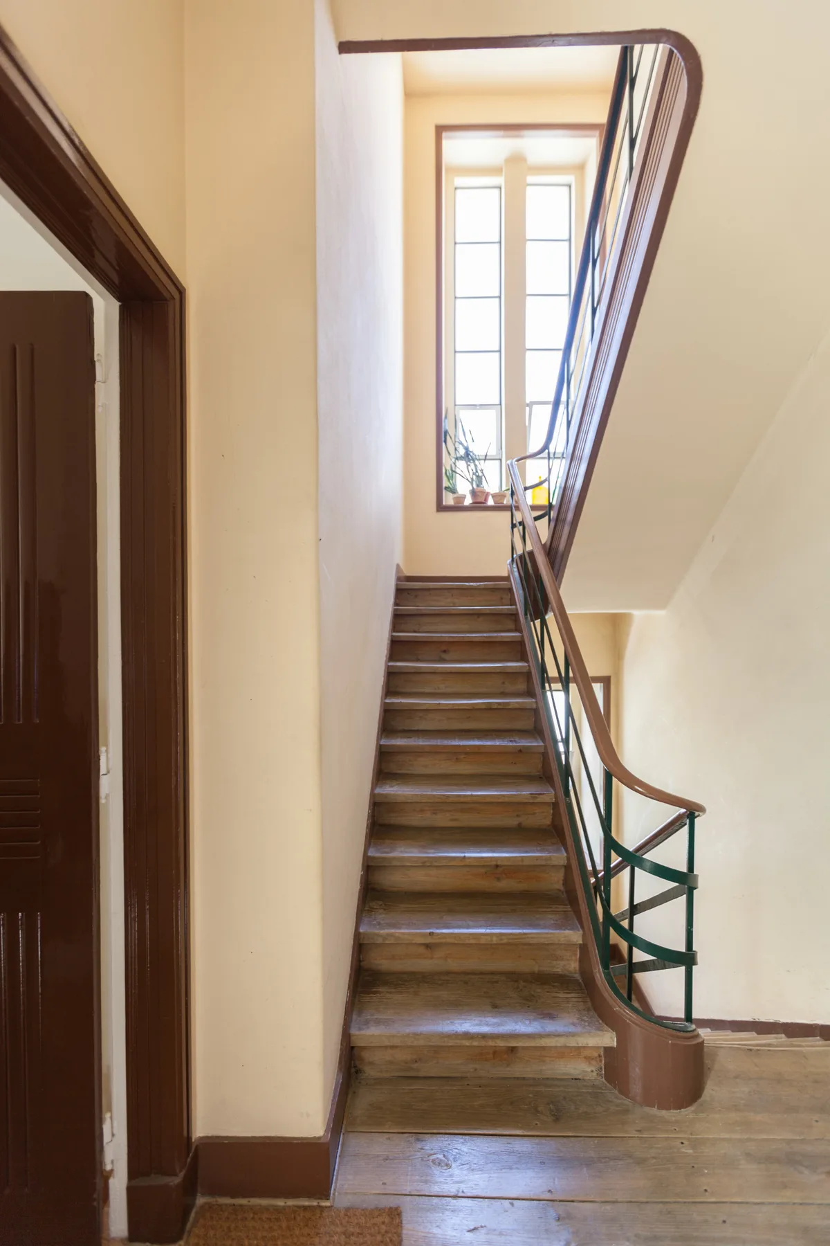 Una escalera de madera con barandilla curva conduce a una ventana luminosa.