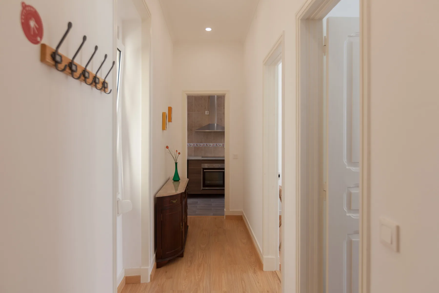 Un pasillo conduce a una cocina, con ganchos para abrigos en la pared.
