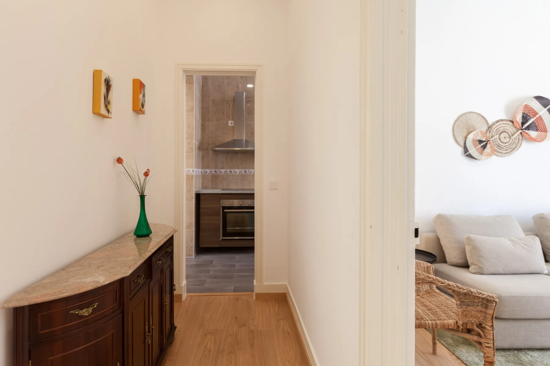 Un pasillo da a una cocina, con una consola de madera y una zona de estar a la vista.