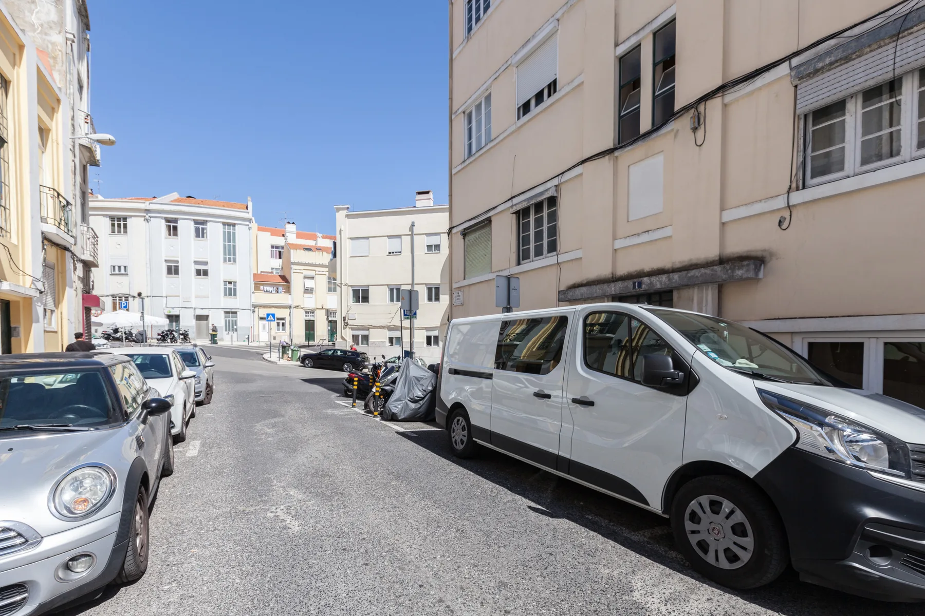 Una calle urbana estrecha con edificios de apartamentos y vehículos estacionados.