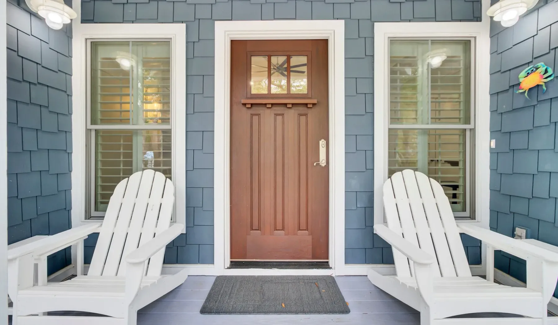 A covered entry porch with a wooden door and white seating.