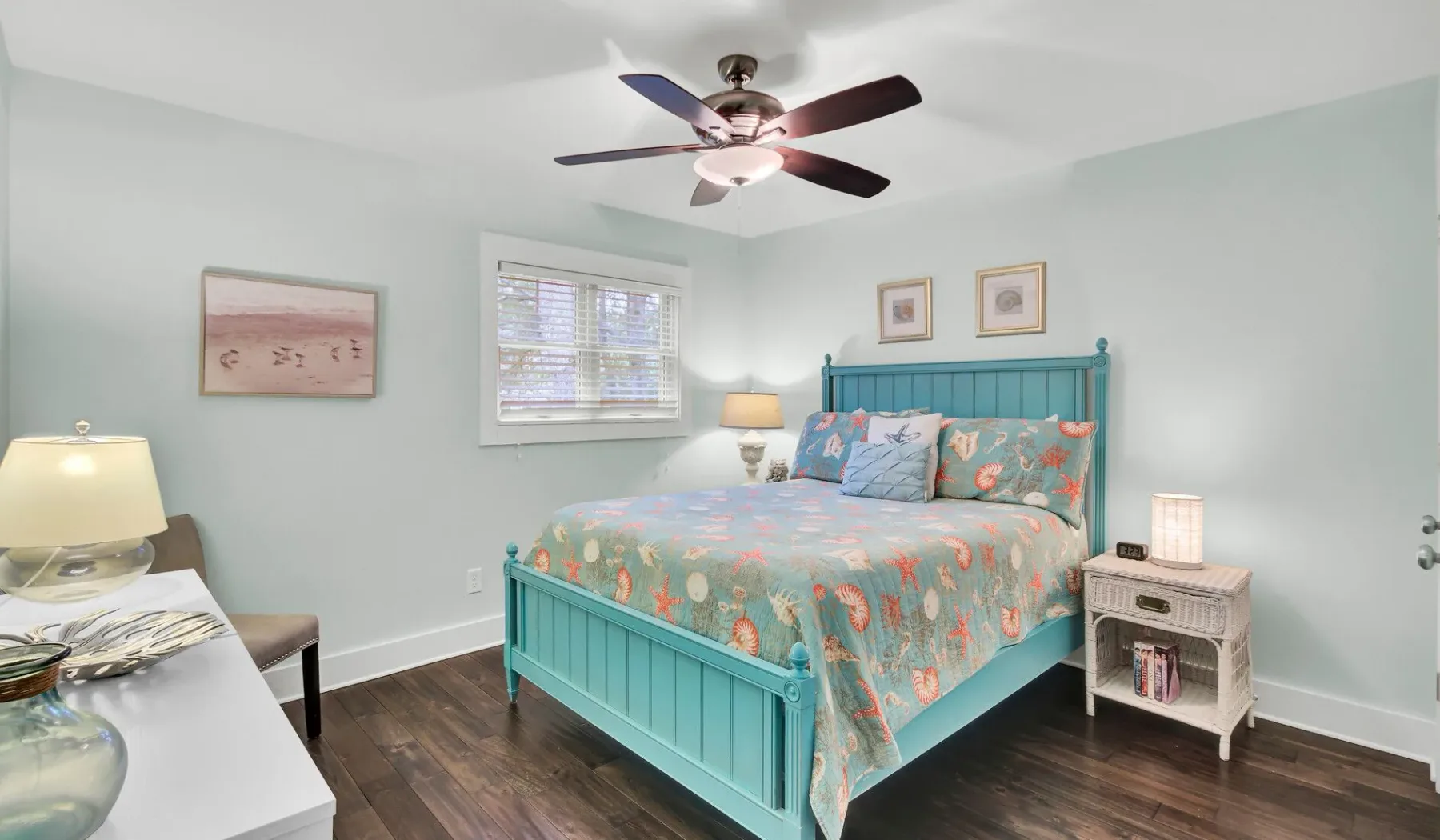 A bedroom with a turquoise bed, patterned bedding, and a ceiling fan.