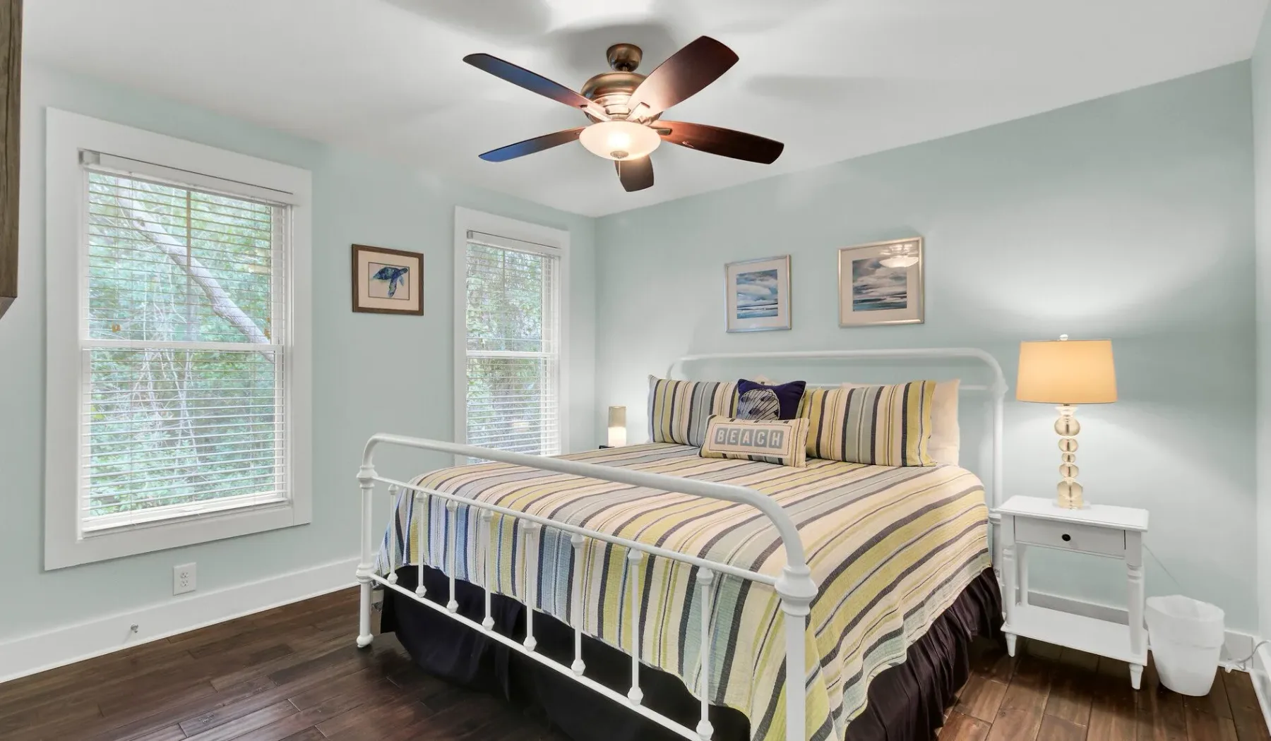 A bedroom with a striped bed, two windows, and a ceiling fan.
