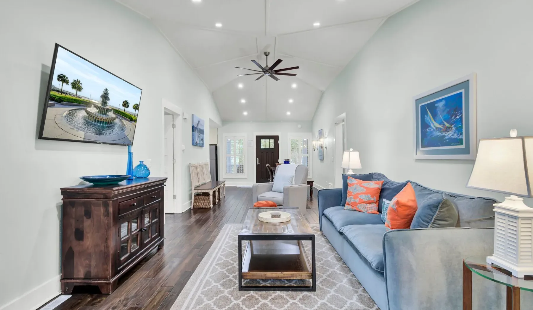 A bright living room with blue seating, a coffee table, and framed artwork.