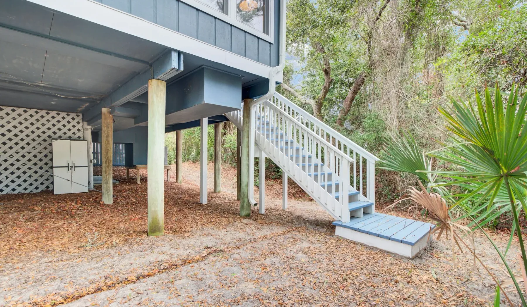 Raised house exterior with a staircase descending to a sandy yard.