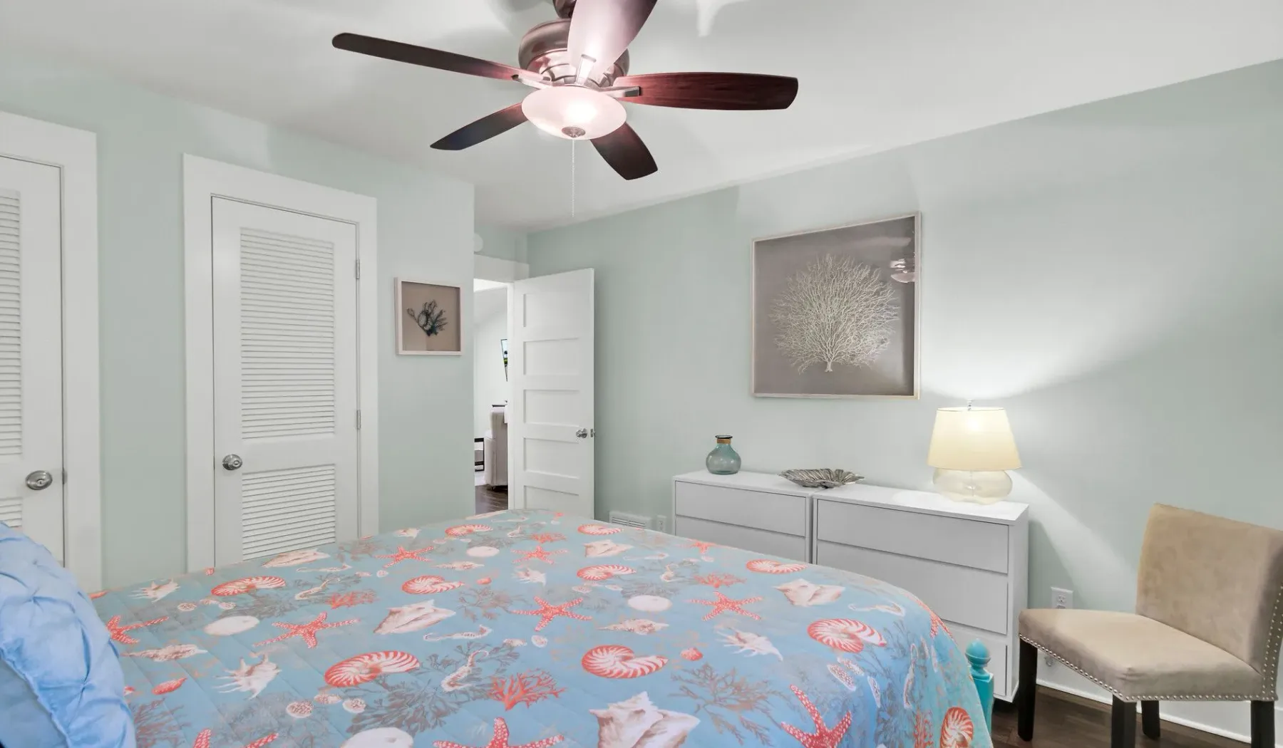 A bedroom with a patterned bedspread, ceiling fan, and dresser.
