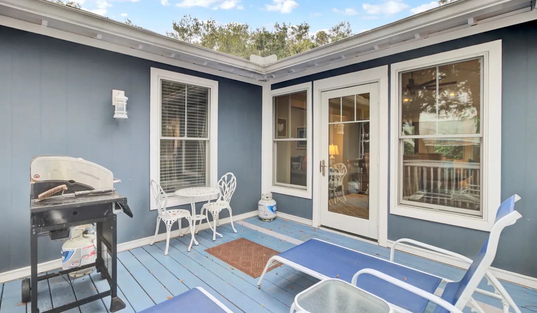 A small outdoor patio with blue decking, seating, and glass doors.