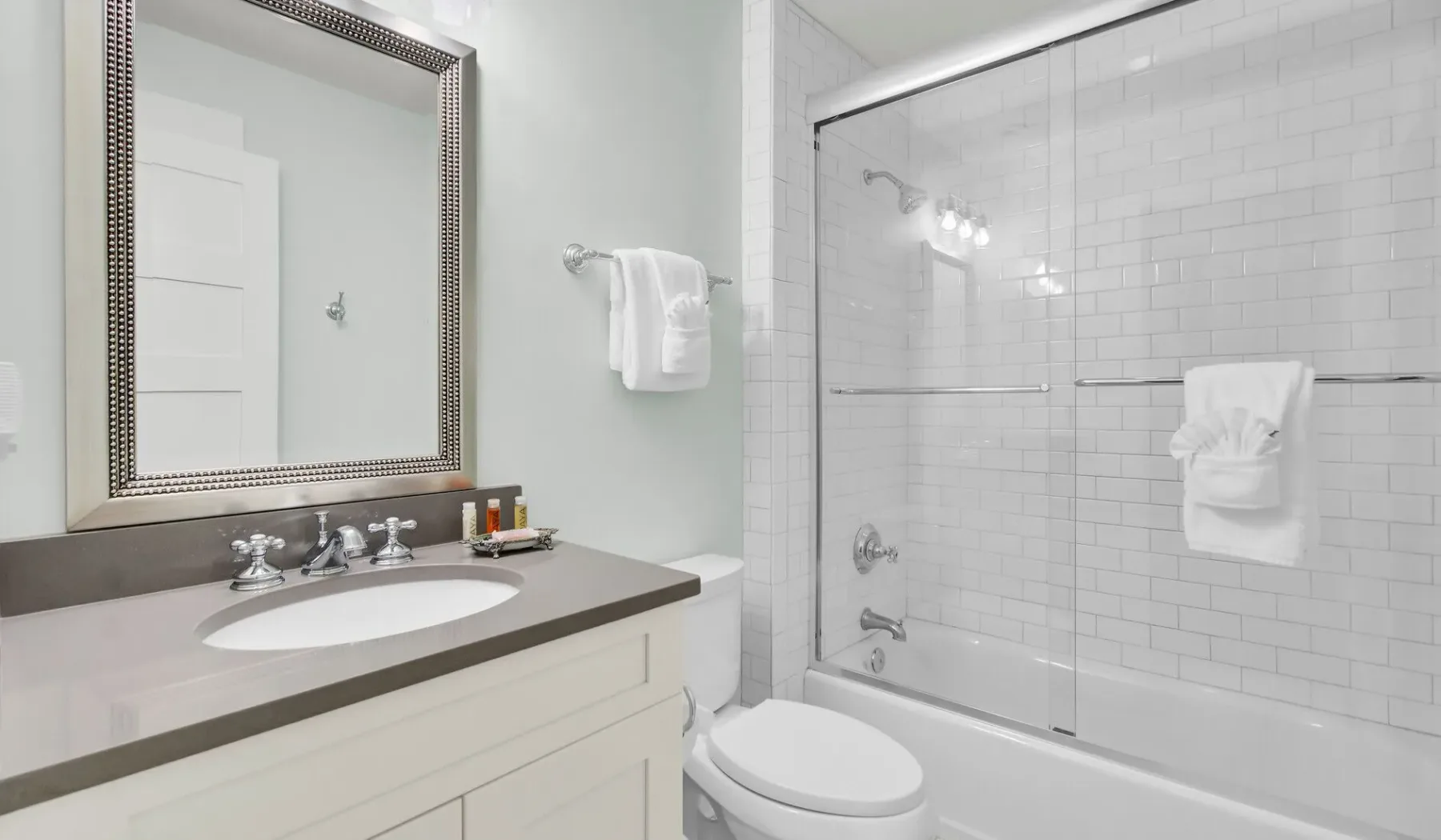 A bright bathroom with a sink, mirror, and tiled shower.