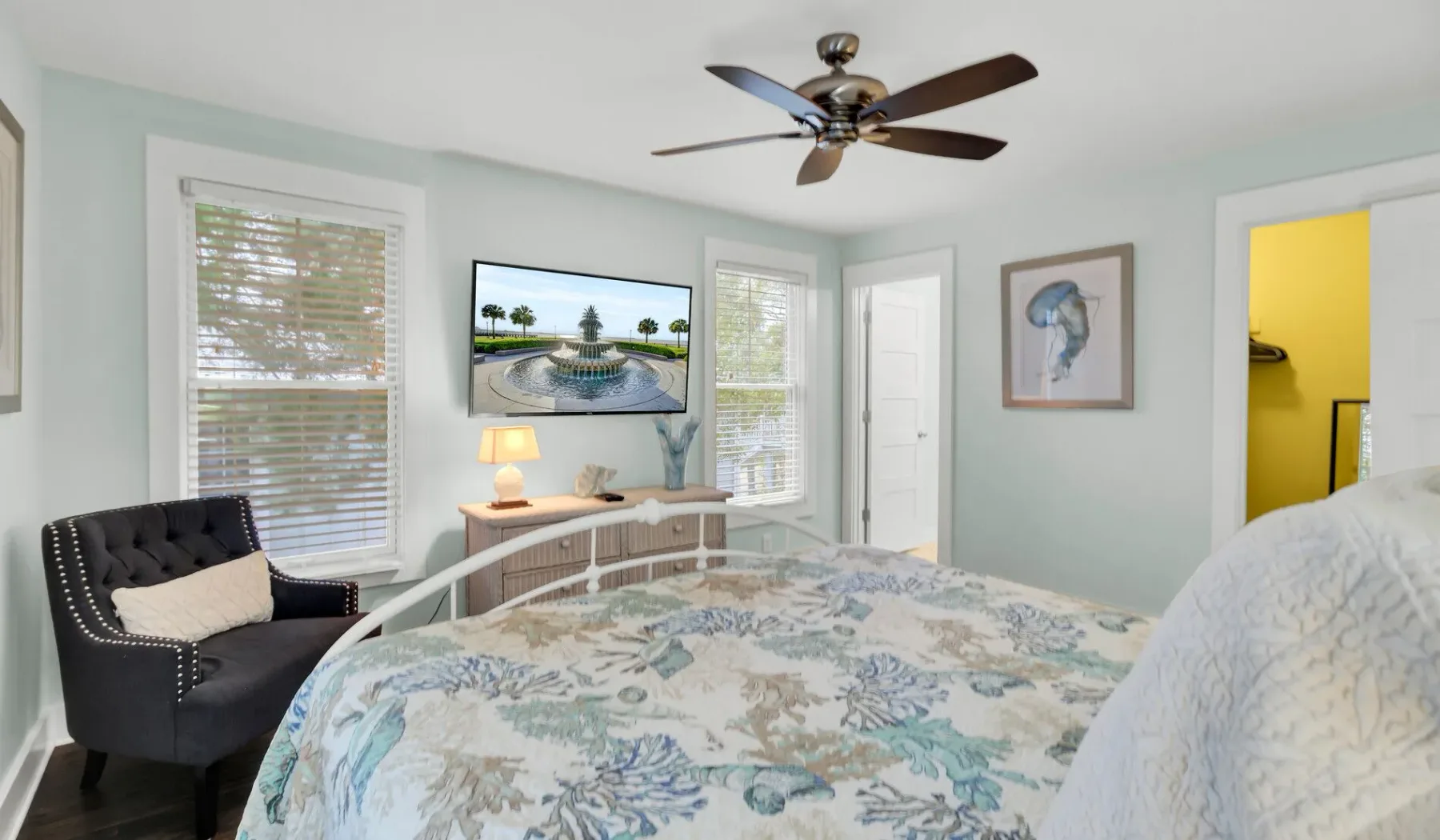 A bedroom with a patterned bedspread, a dark armchair, and a ceiling fan.