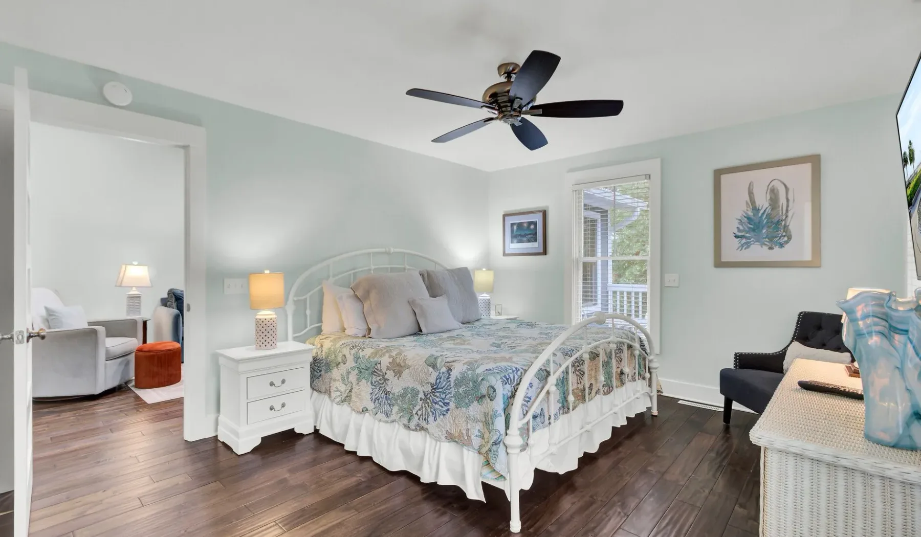 A bright bedroom with a floral bedspread and a ceiling fan.