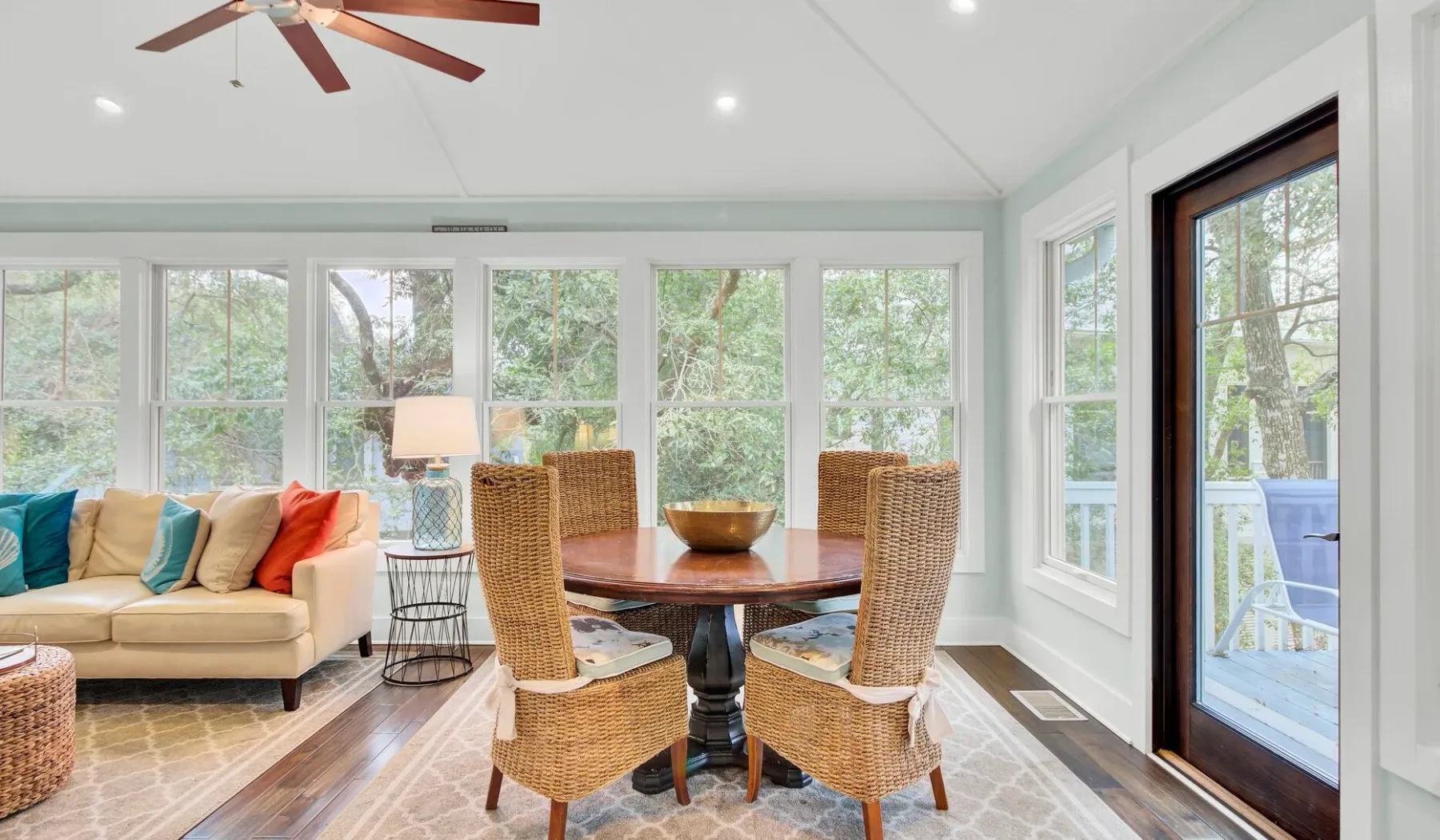 A bright sunroom with a round dining table, wicker seating, and large windows.