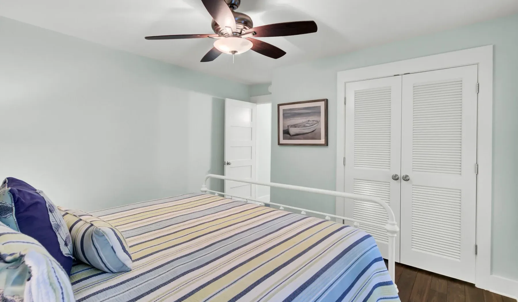 A bedroom with a striped bedspread, wall art, and a ceiling fan.
