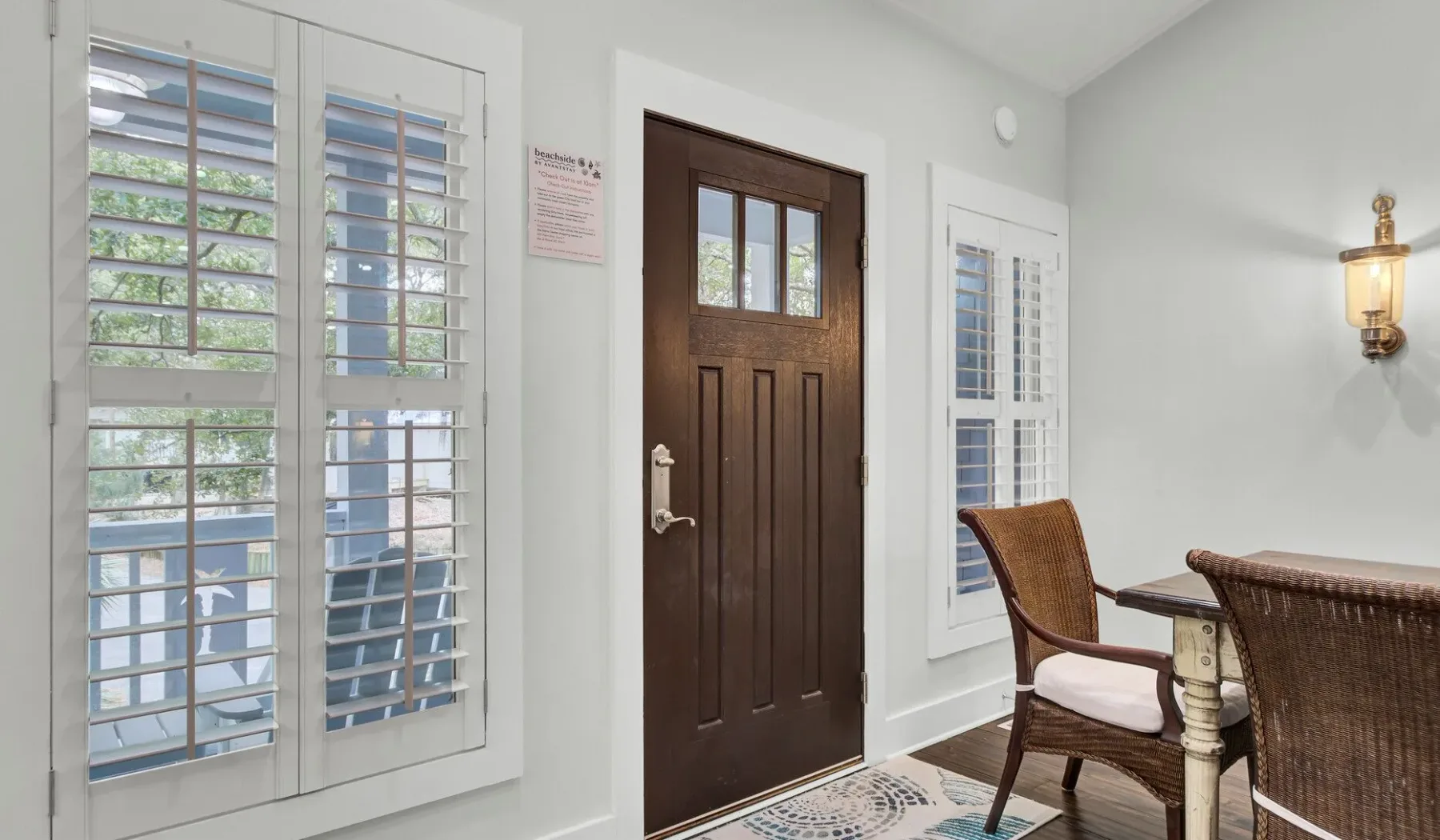 A bright entryway with a dark wooden door and shuttered windows.
