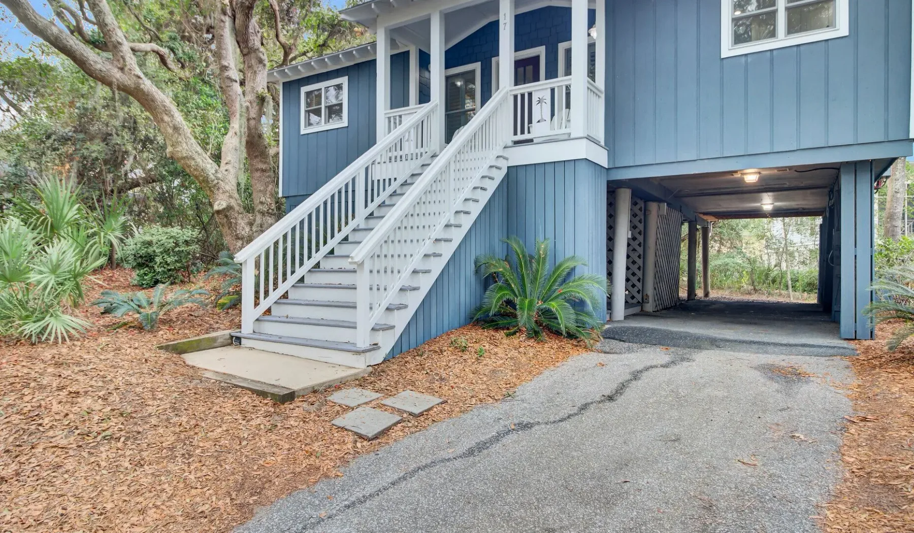 Blue raised house with white exterior stairs and a driveway beneath.