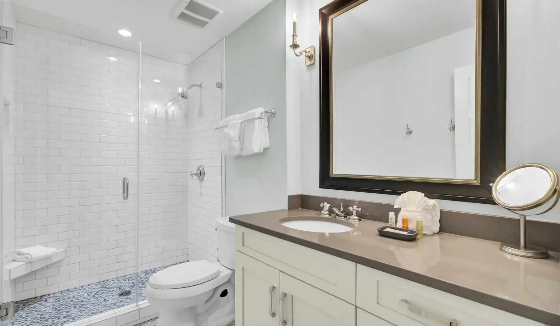 A bright bathroom with a tiled shower and a long vanity.