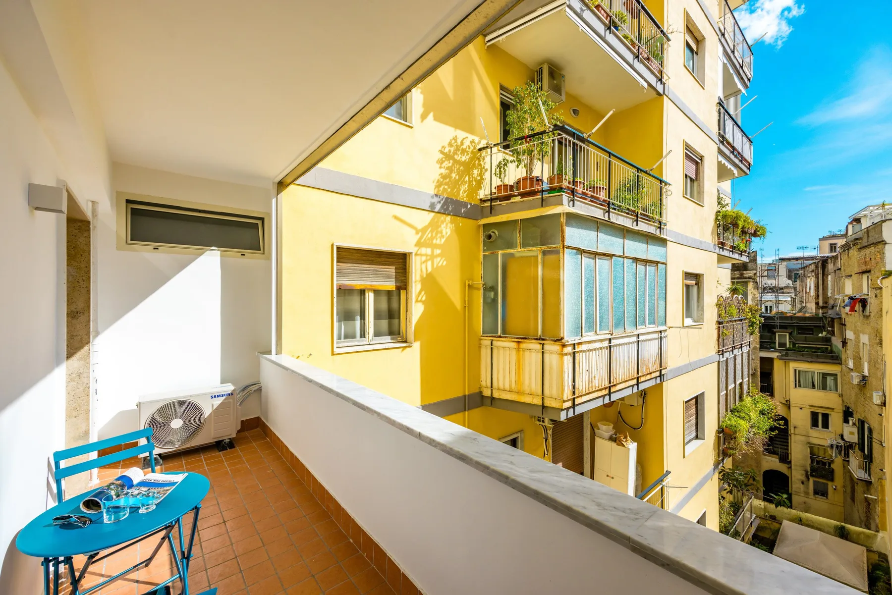 A tiled balcony overlooks a yellow apartment building and the surrounding city.