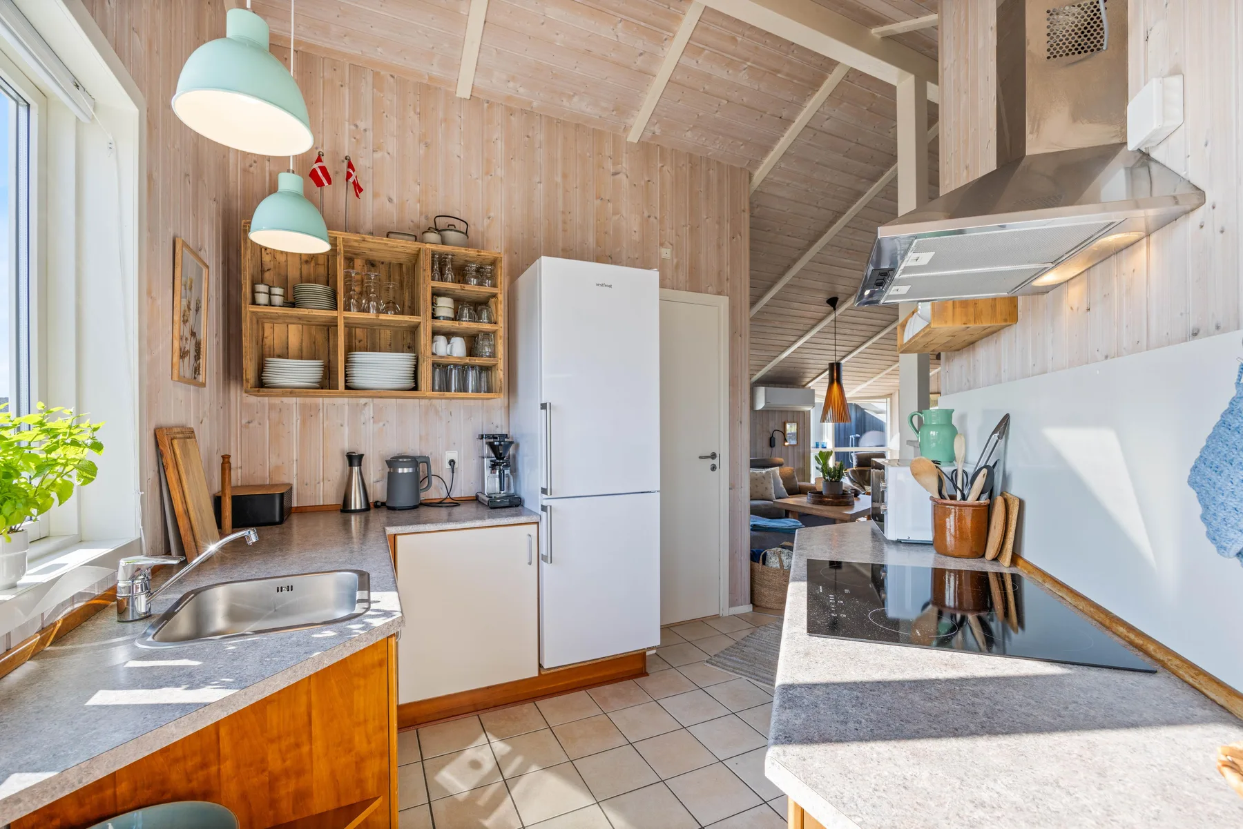 Una cocina revestida de madera con un refrigerador central y una zona de cocción en la encimera.