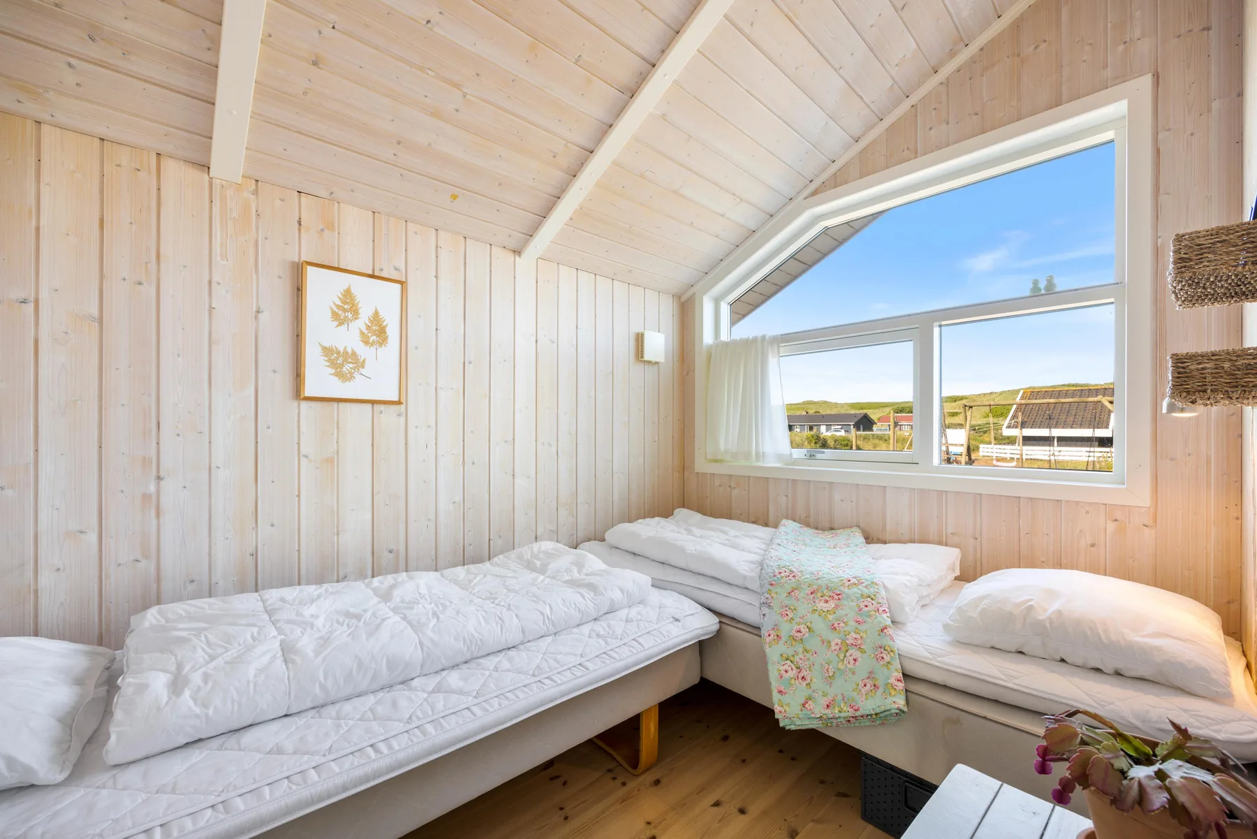 Un dormitorio luminoso con dos camas bajo una gran ventana inclinada.