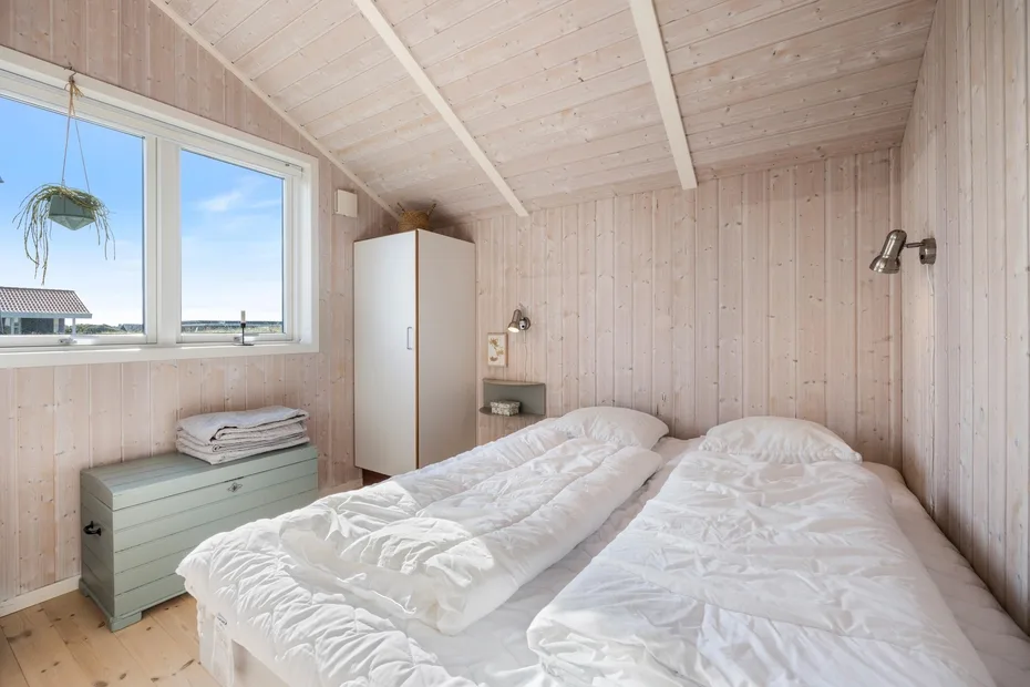 Un dormitorio luminoso con dos camas, paredes de madera clara y una ventana grande.