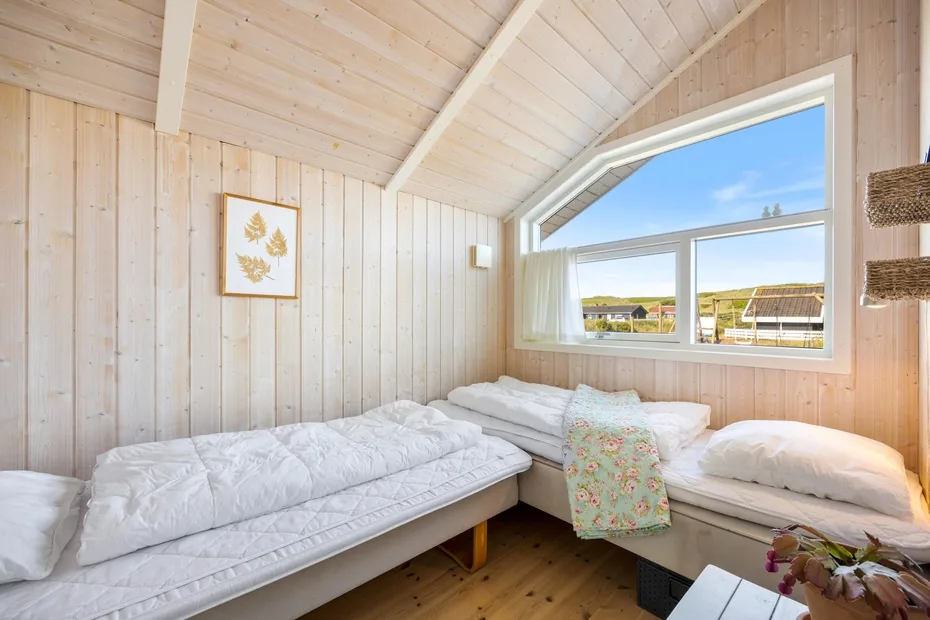 Un dormitorio luminoso con dos camas bajo una gran ventana inclinada.