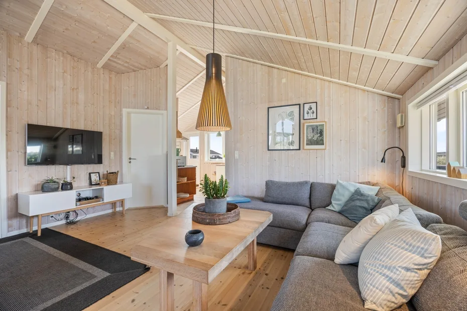 Una sala luminosa con asientos grises, una mesa de centro de madera y un televisor en la pared.