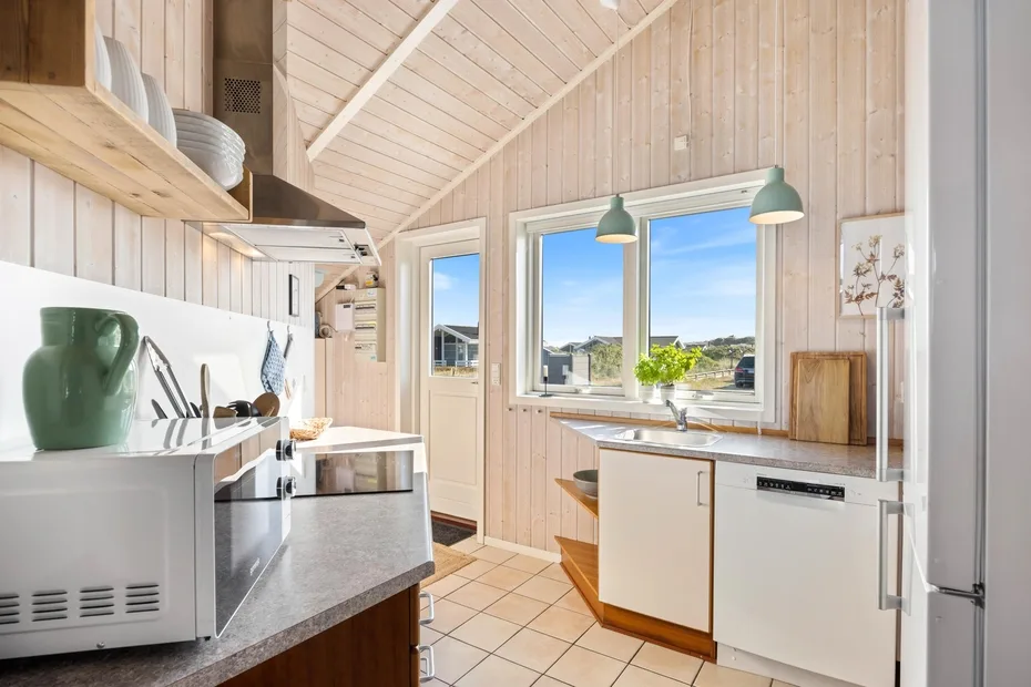 Una cocina luminosa con gabinetes blancos, una encimera y ventanas grandes.