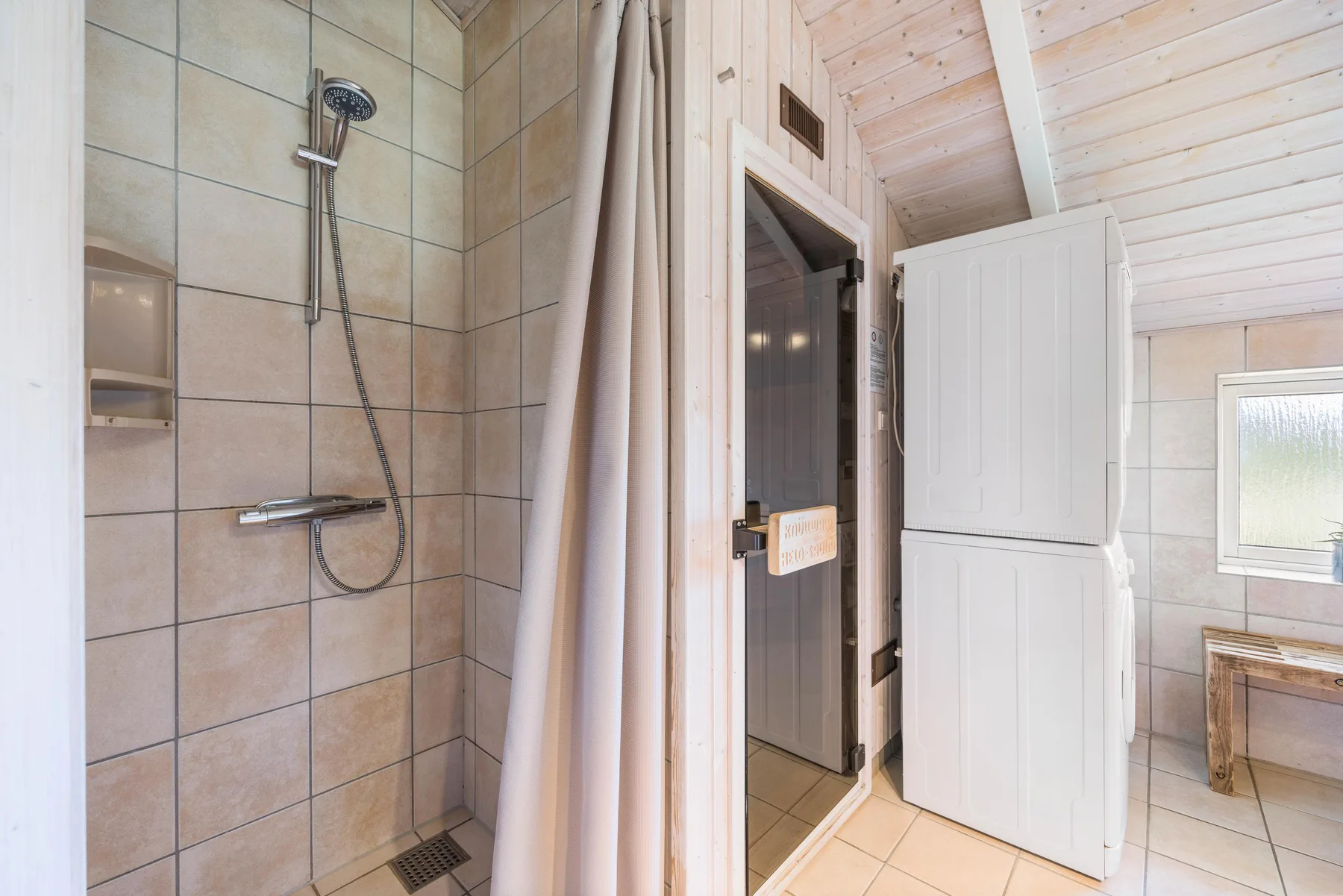 Un baño alicatado con ducha junto a una sauna con frente de vidrio.