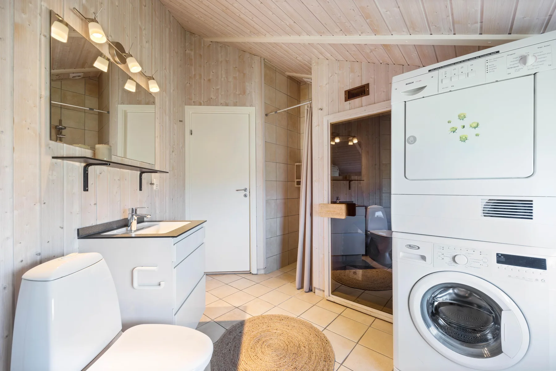 Un baño con lavabo, inodoro y electrodomésticos de lavandería apilados.