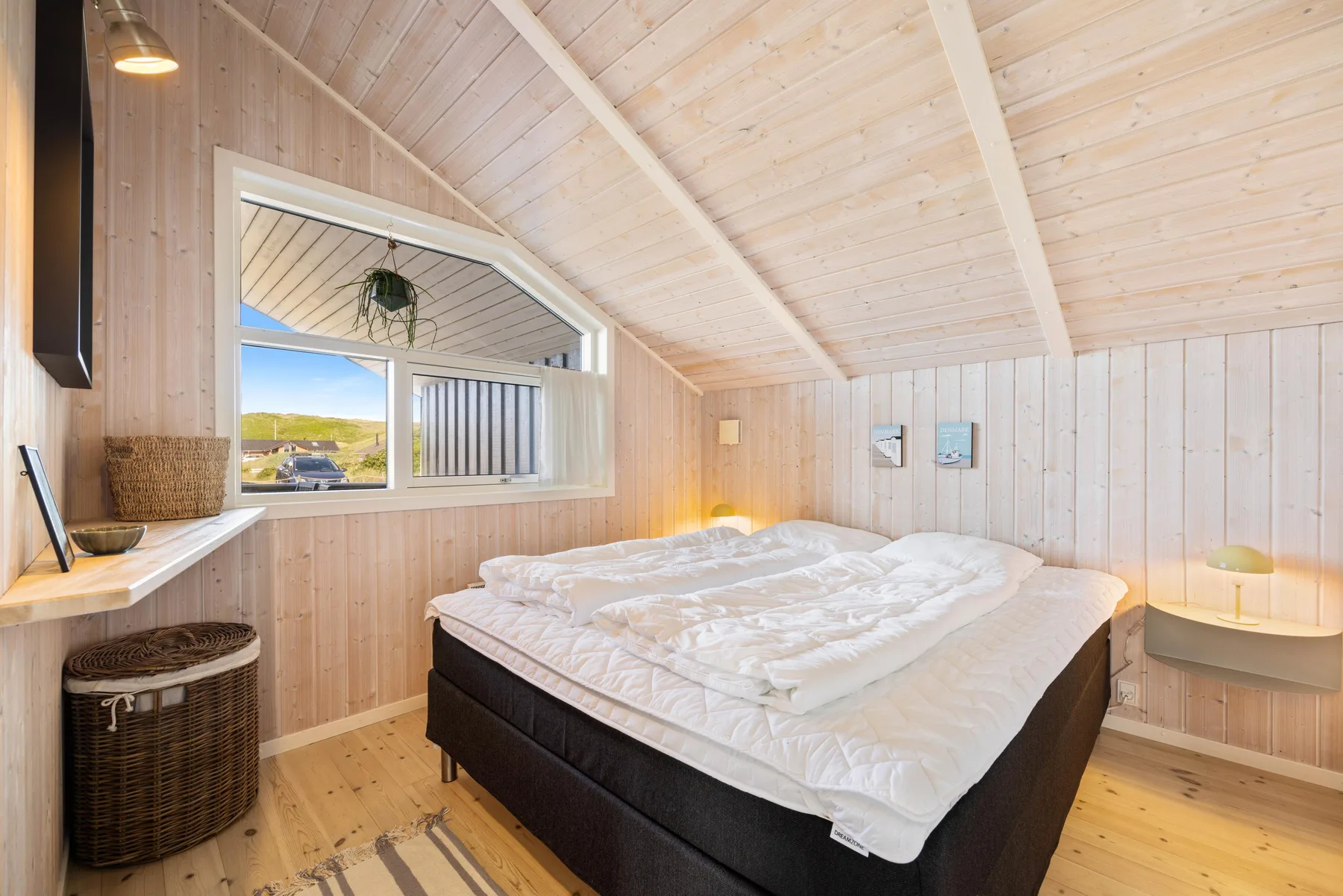 Un dormitorio con una cama grande bajo un techo inclinado de madera clara.