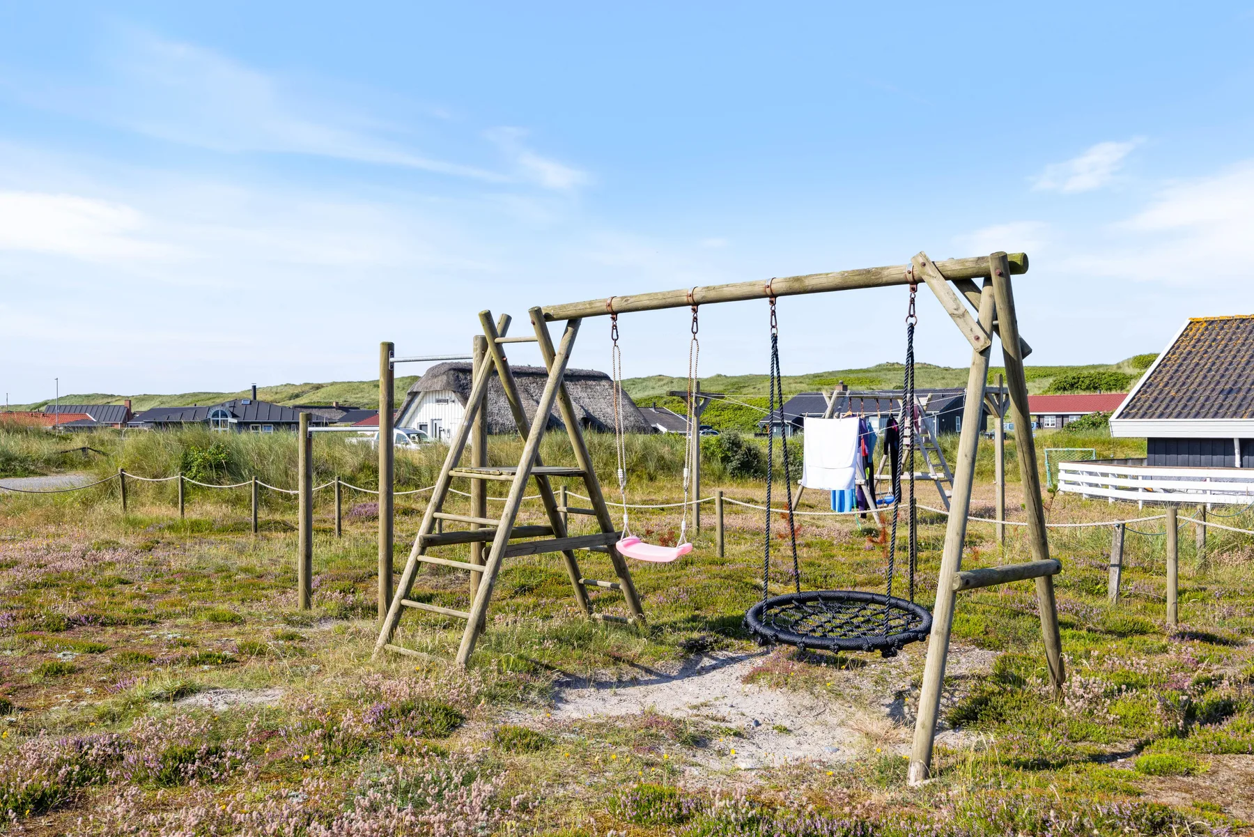 Una zona de juegos al aire libre con columpios de madera está entre dunas cubiertas de hierba.