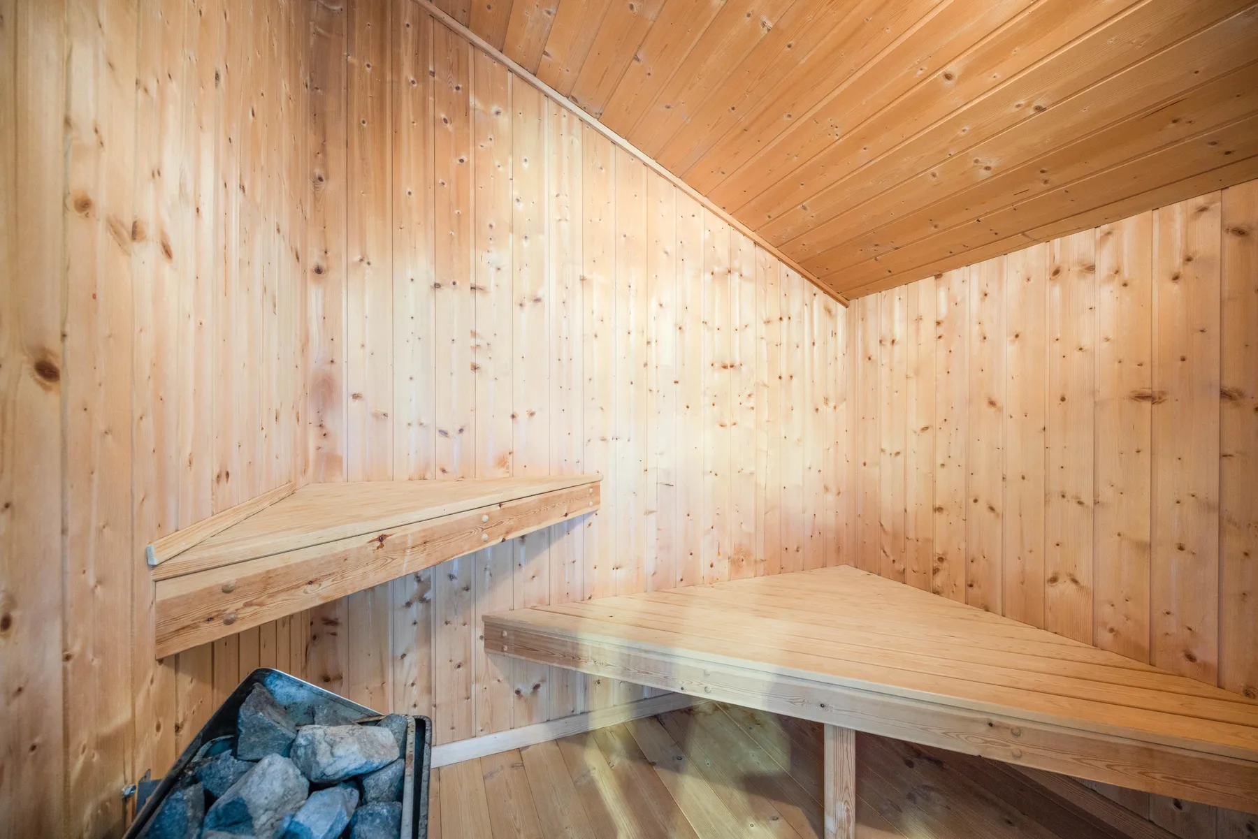 Una sauna revestida de madera con bancos escalonados y una estufa con piedras.