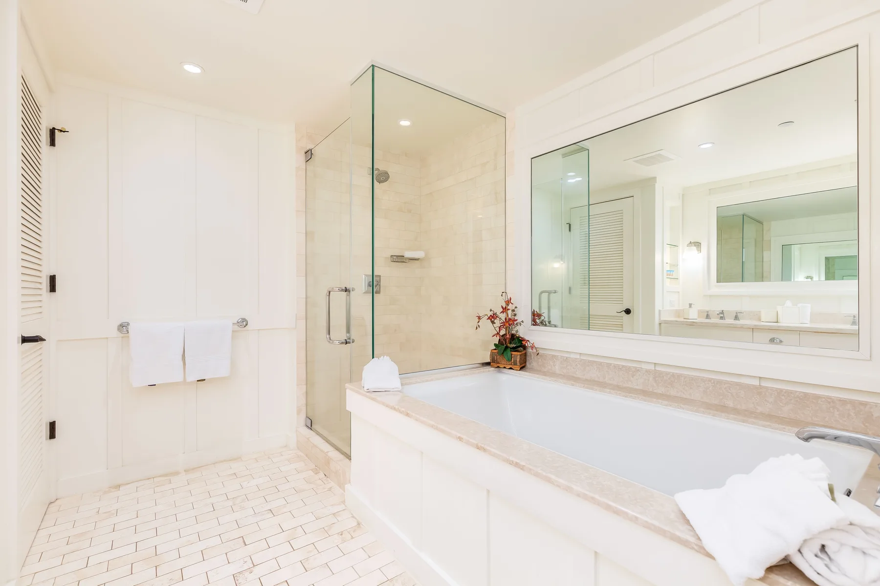 A bright bathroom with a bathtub, glass shower, and large wall mirror.