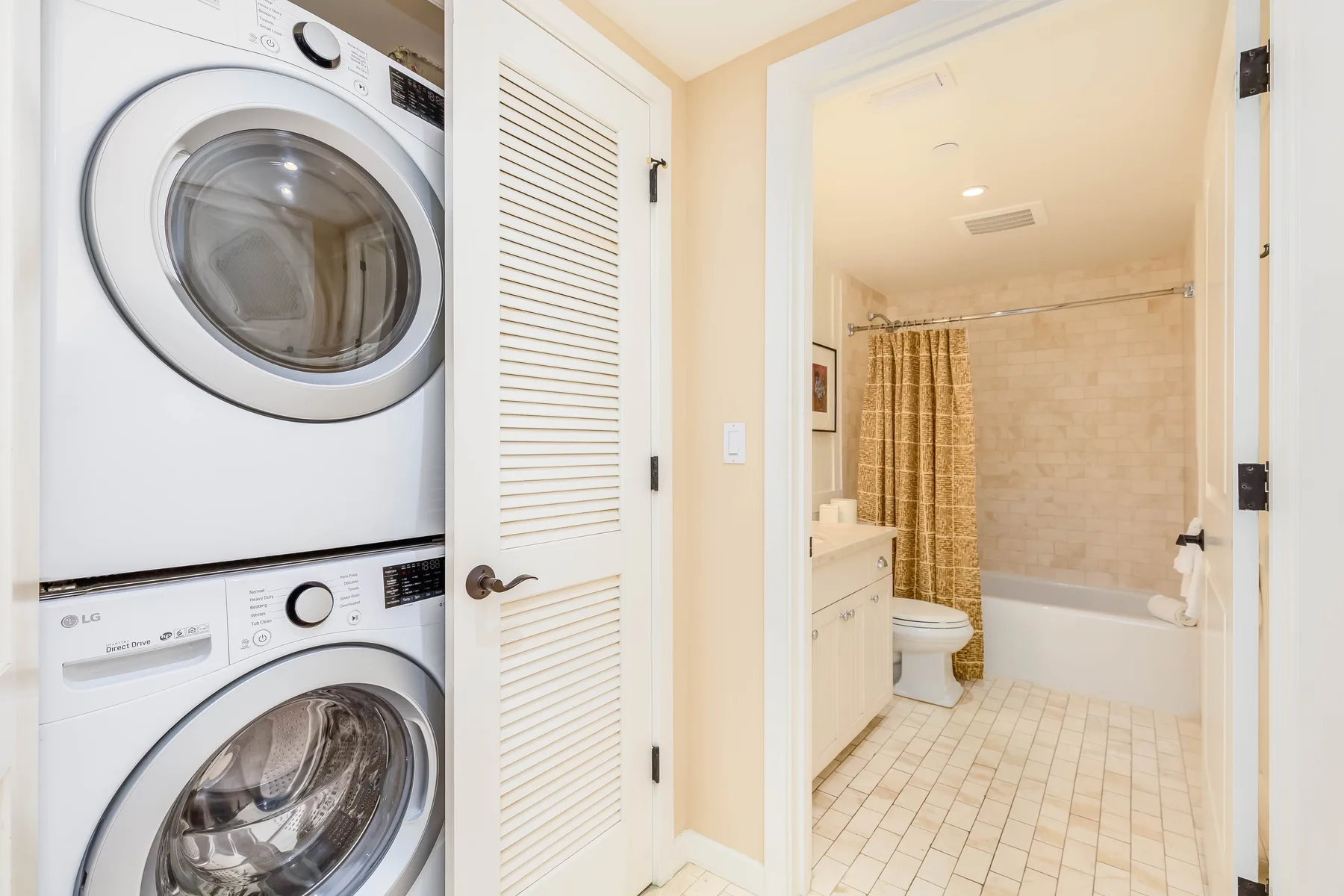 A bathroom with a bathtub and shower curtain, beside a stacked washer and dryer.