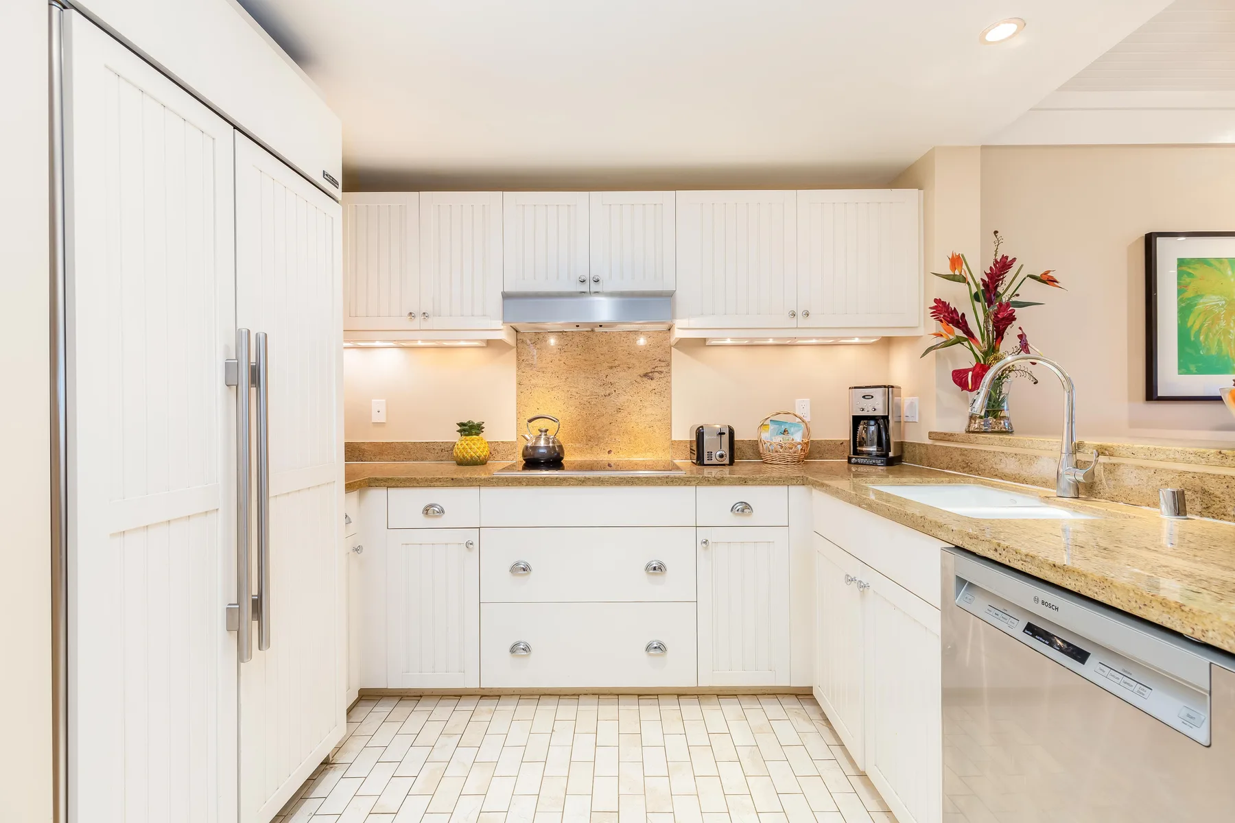 A bright white kitchen with cabinetry, a cooktop, and stone countertops.