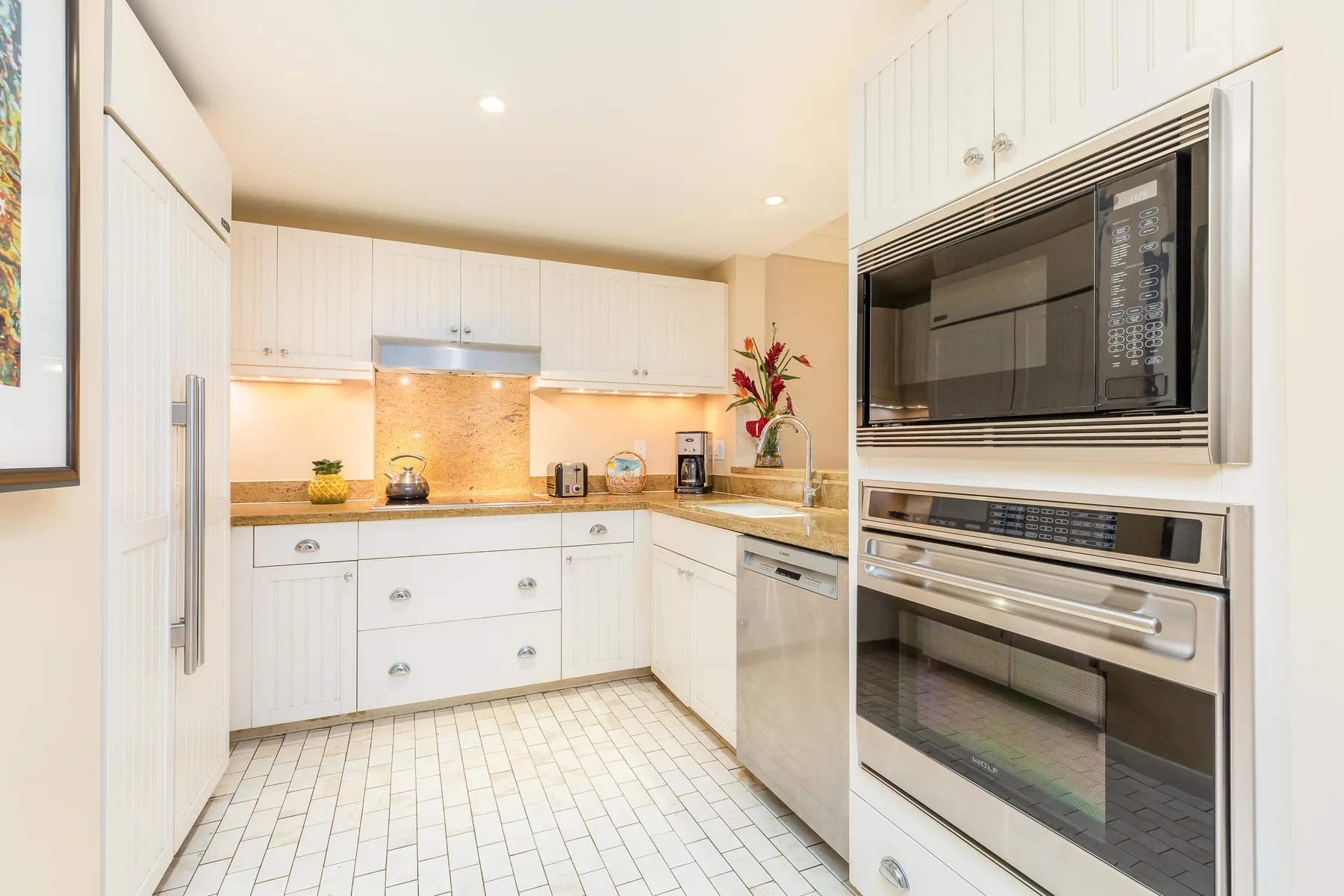 Una cocina luminosa con gabinetes blancos, salpicadero de azulejos y electrodomésticos de acero inoxidable.
