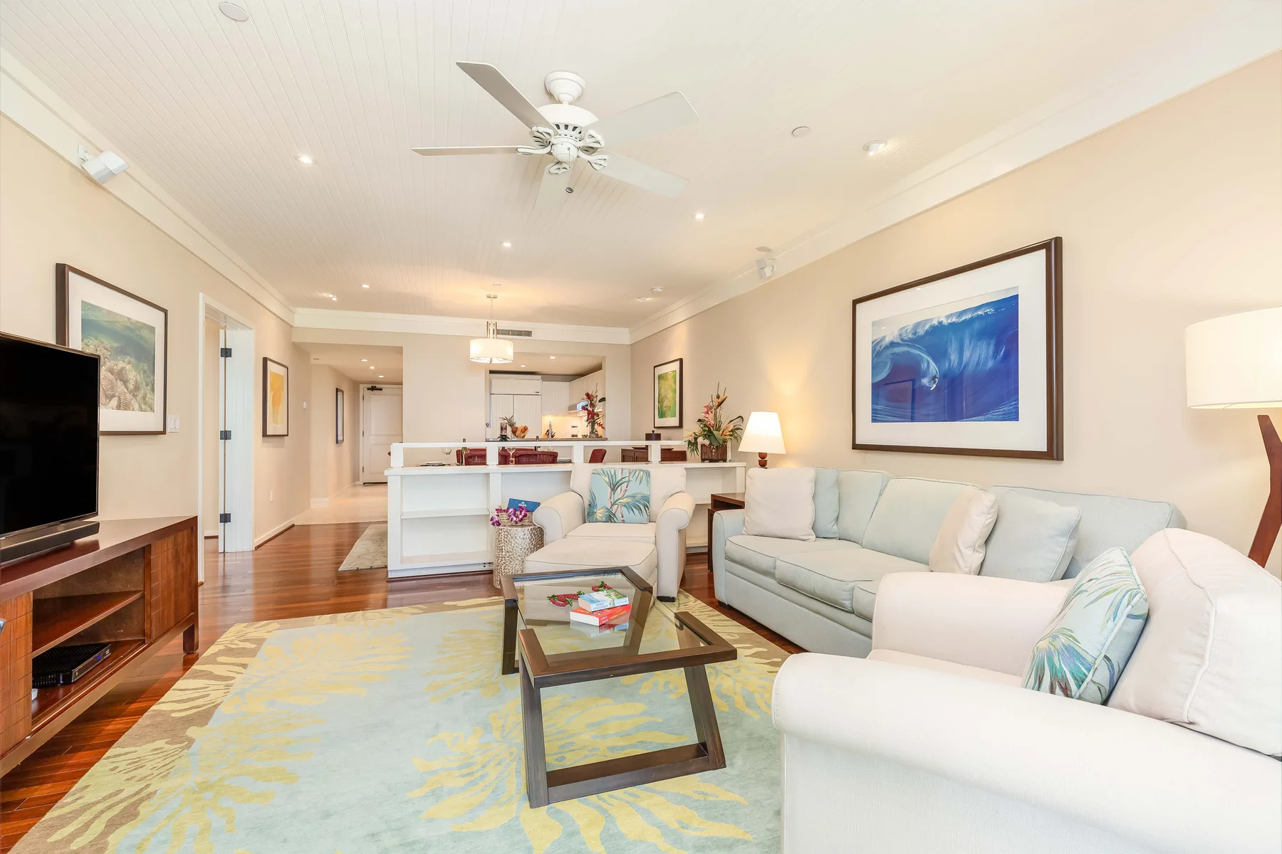 A bright living room with pale seating, a coffee table, and a ceiling fan.
