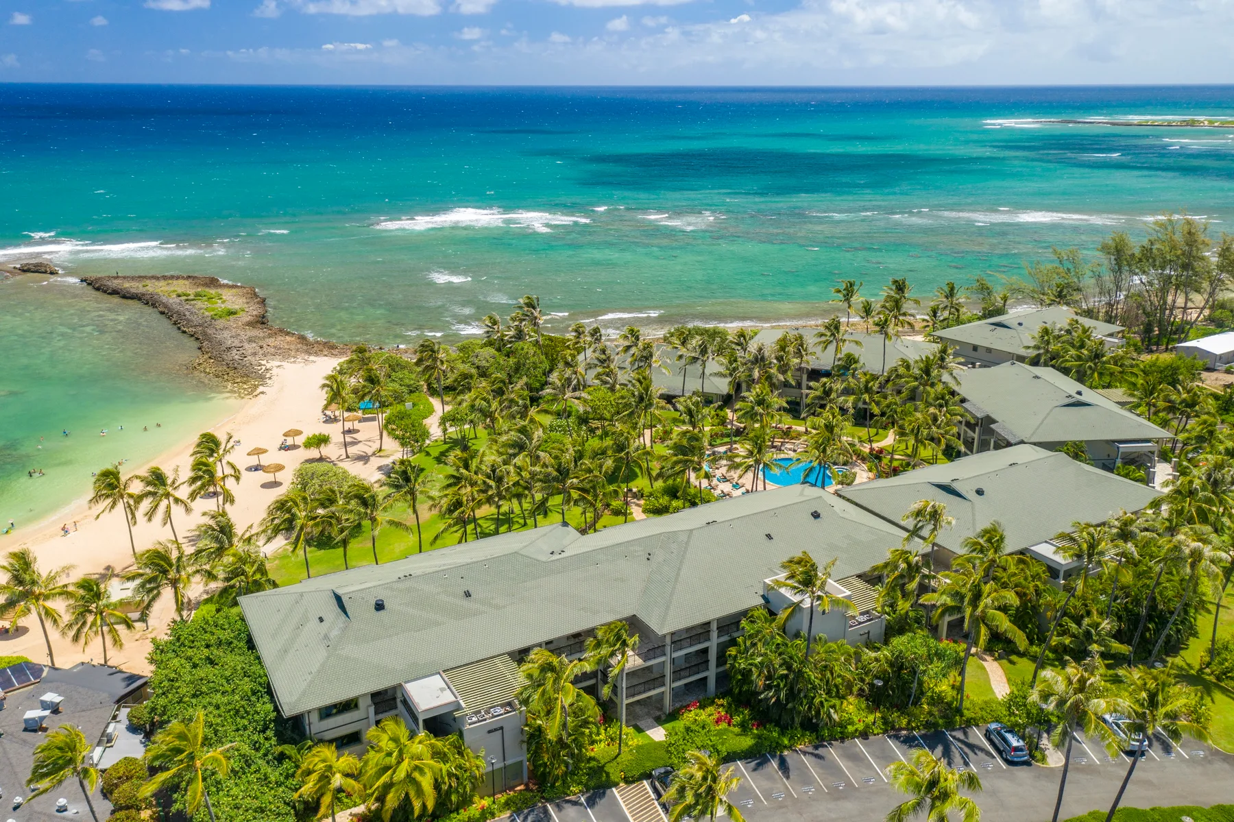 Aerial view of a palm-lined coastal resort beside turquoise water and a sandy beach.