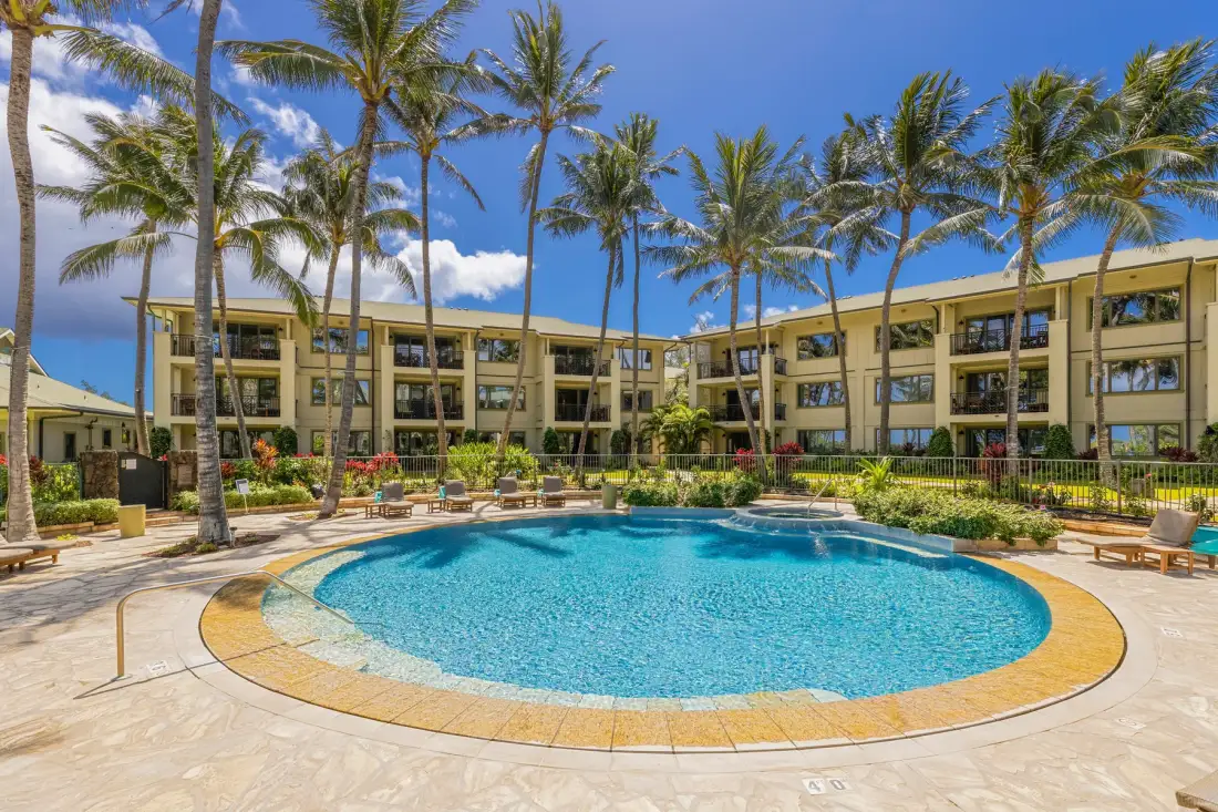 An outdoor swimming pool is surrounded by palm trees and a hotel building.