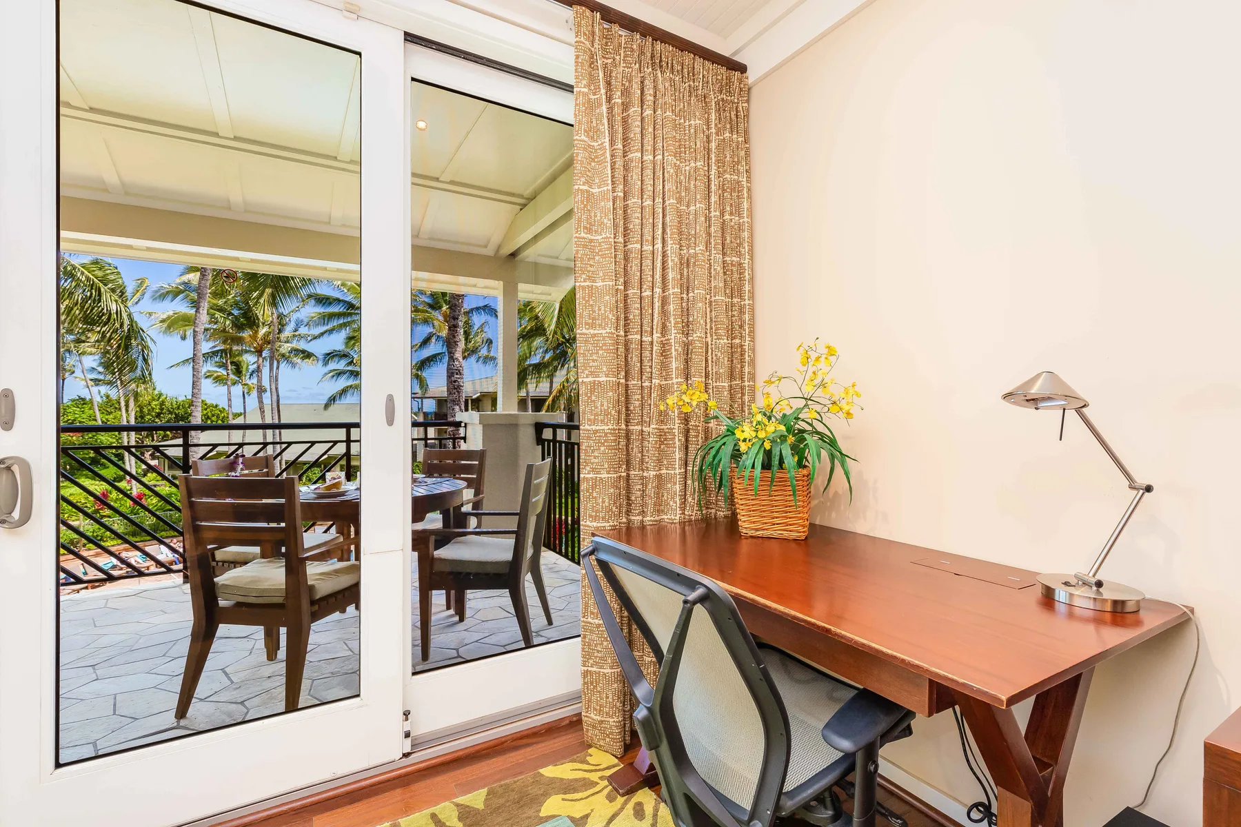 A desk and chair sit beside sliding glass doors opening onto a palm-lined patio.