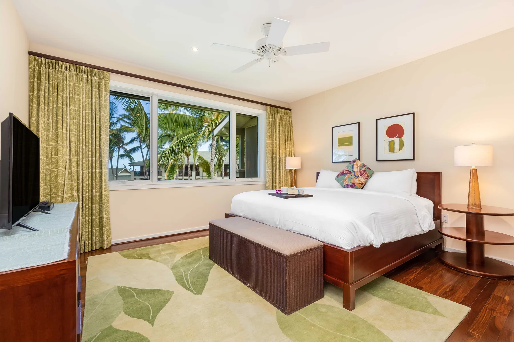 A bright bedroom with a large bed and a window overlooking palm trees.