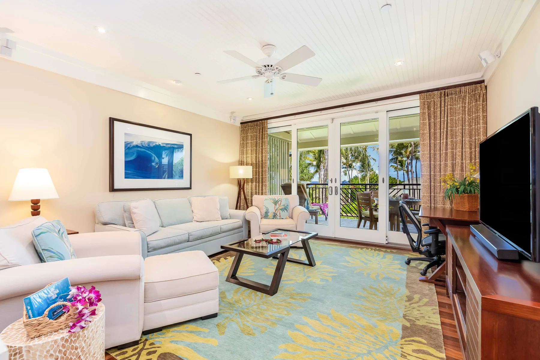 A bright living room with pale seating, a coffee table, and glass doors opening to a balcony.