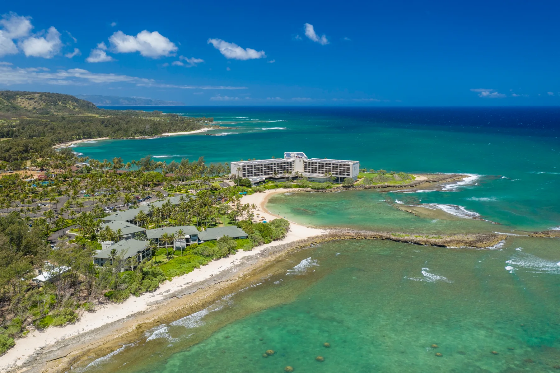 Aerial coastal scene showing a resort beside turquoise water and a sandy shoreline.