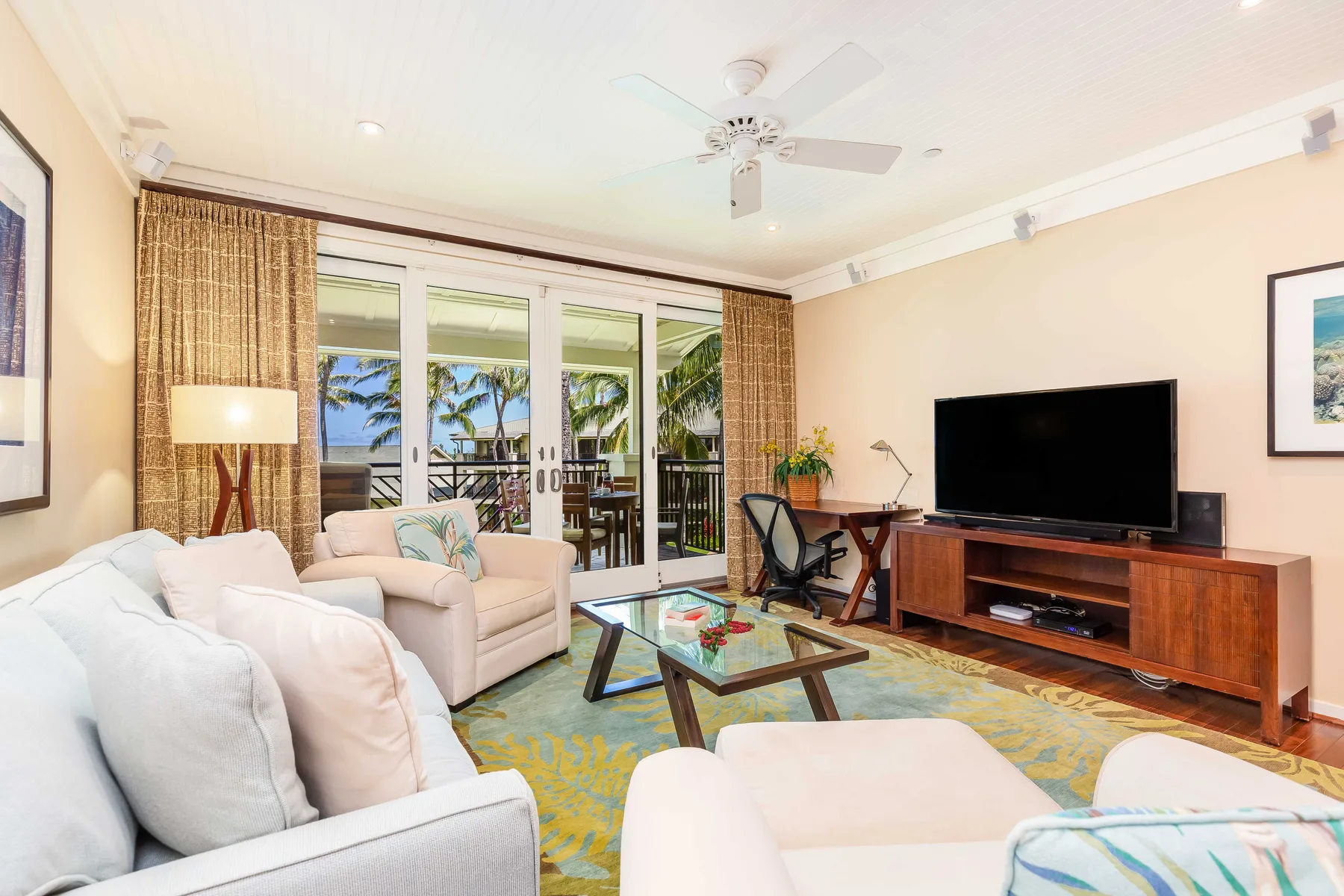 A bright living room with seating, a television, and glass doors opening to a balcony.