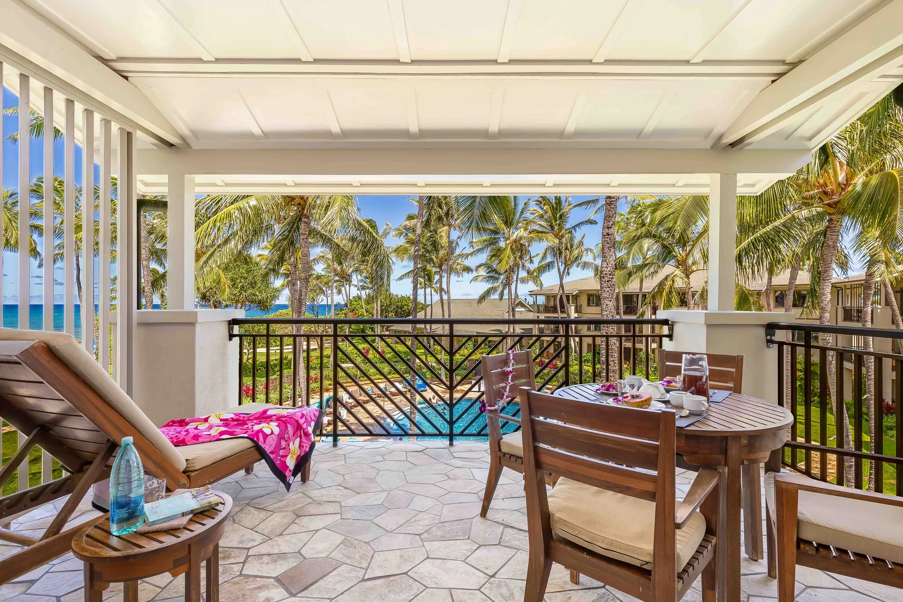 Un patio cubierto con asientos de comedor da a una piscina y palmeras.
