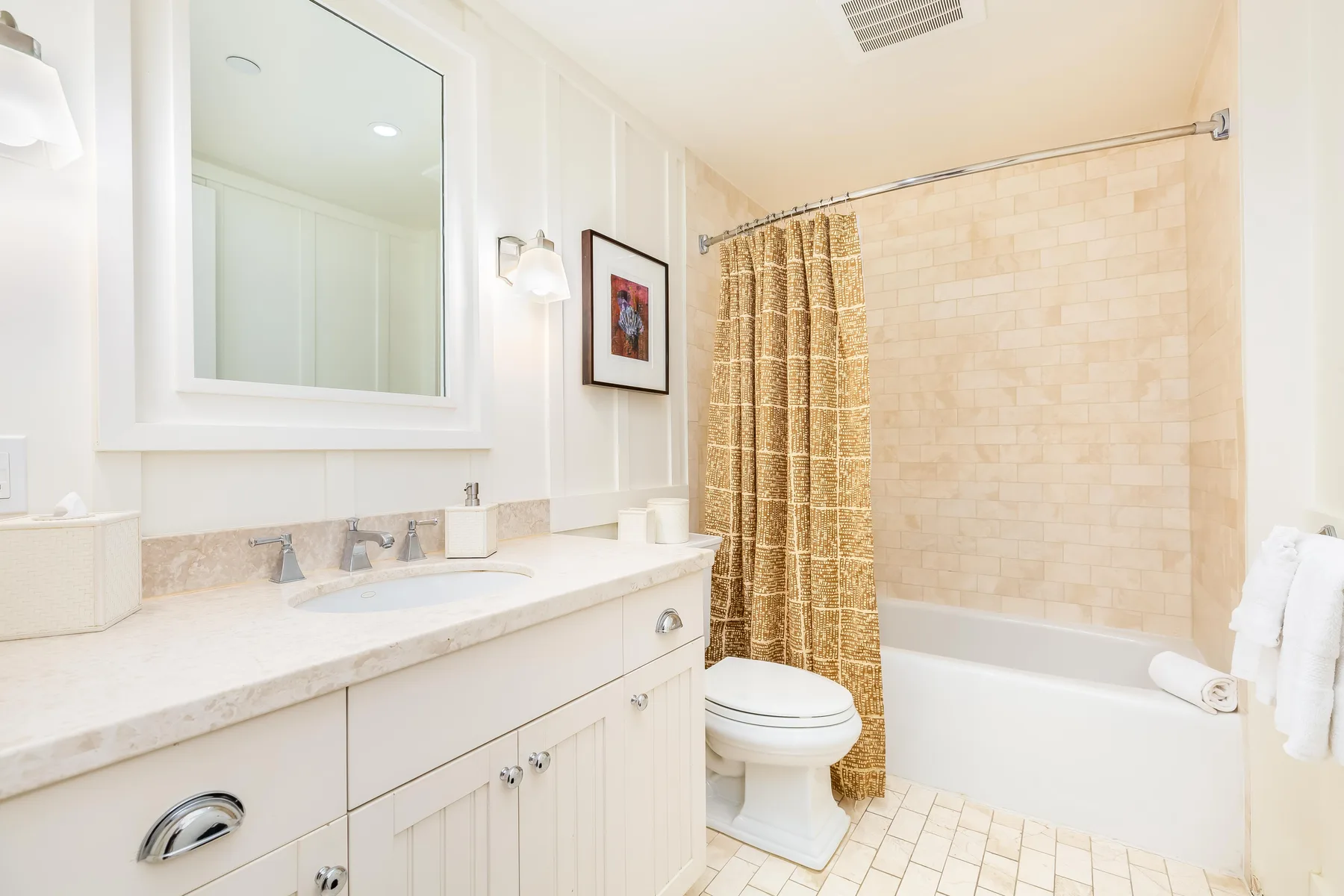 A bright bathroom with a sink vanity, toilet, and bathtub behind a curtain.