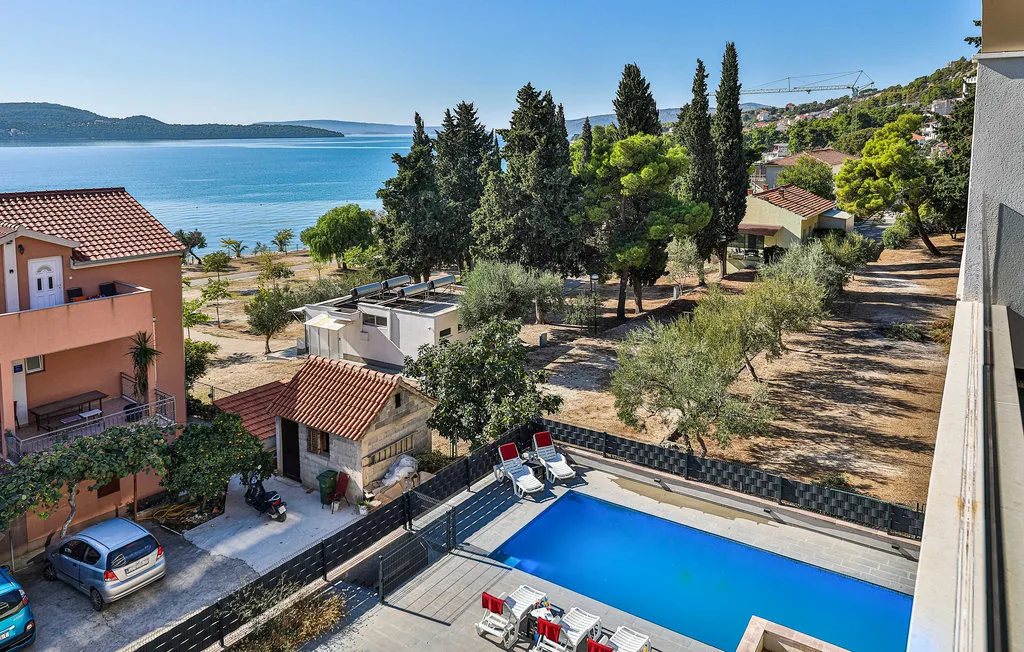 Una piscina y casas cercanas miran al mar y a una ladera arbolada.