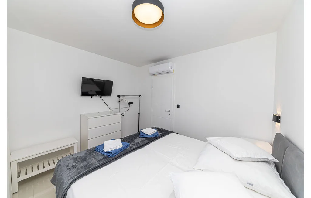 Un dormitorio luminoso con una cama bien tendida y un televisor en la pared.