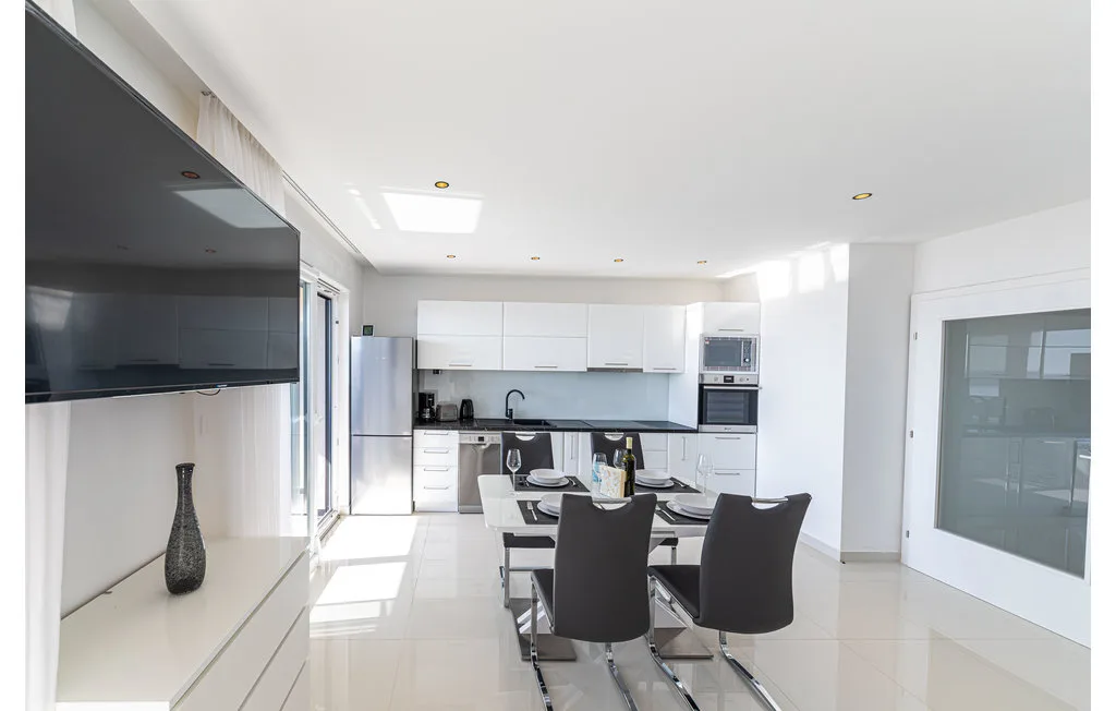 Una cocina luminosa con zona de comedor, mesa, asientos oscuros y armarios blancos.